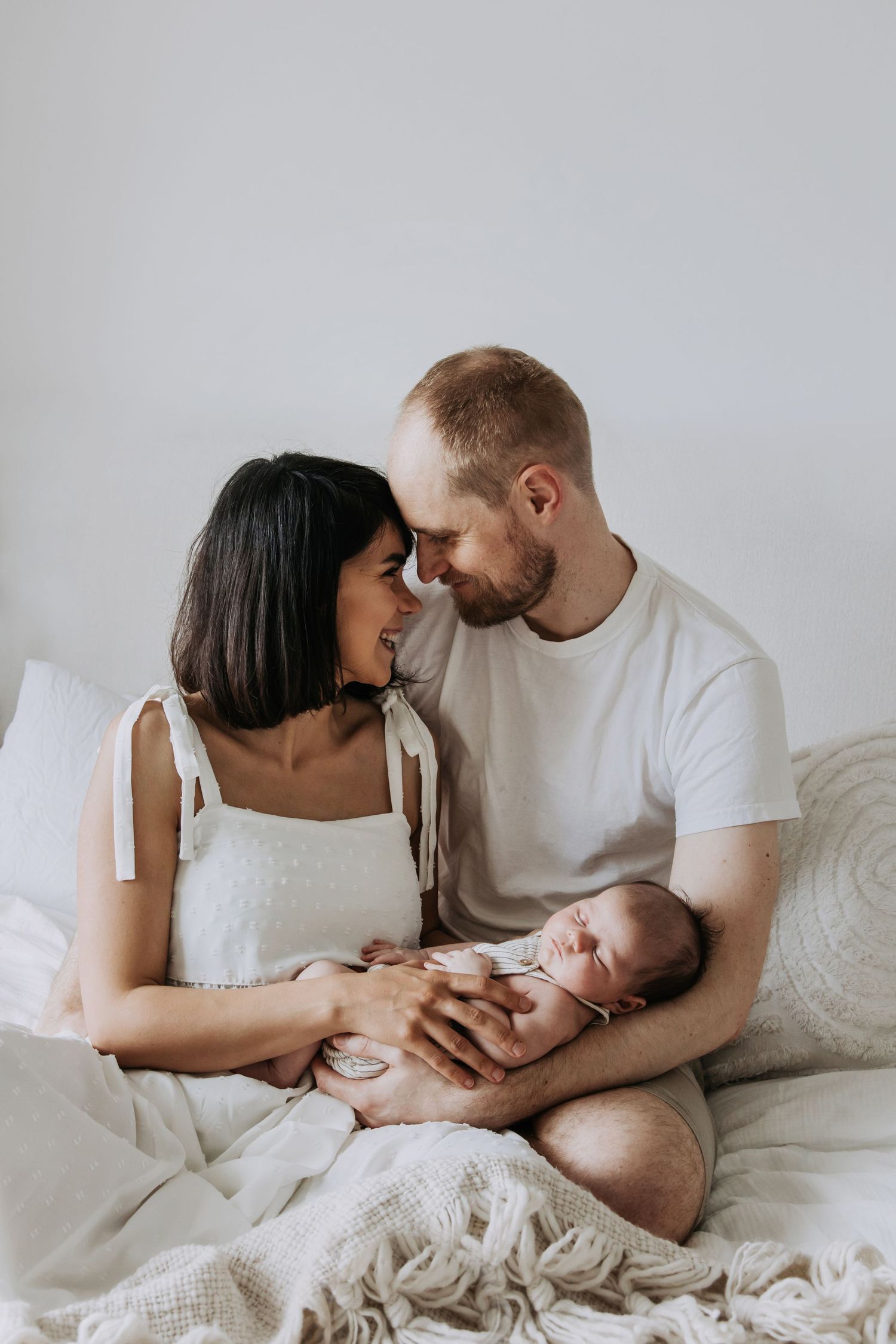 Parents smiling at each other while holding their sleeping newborn baby during an in-home lifestyle newborn photography session in Bath.
