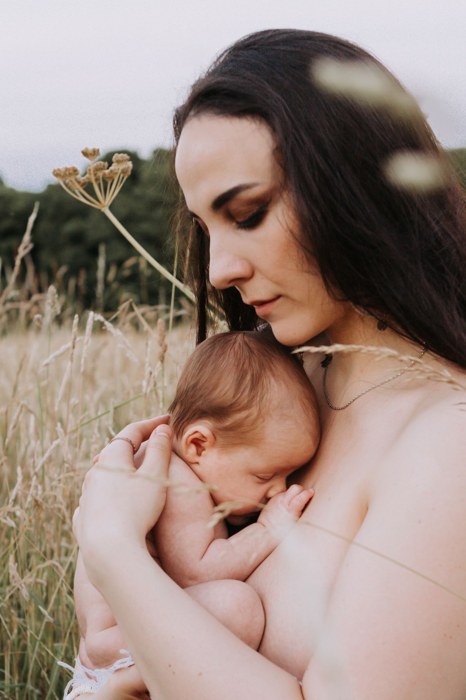 Close-up of a mother cuddling and breastfeeding her sleeping newborn baby outdoors in a grassy field.