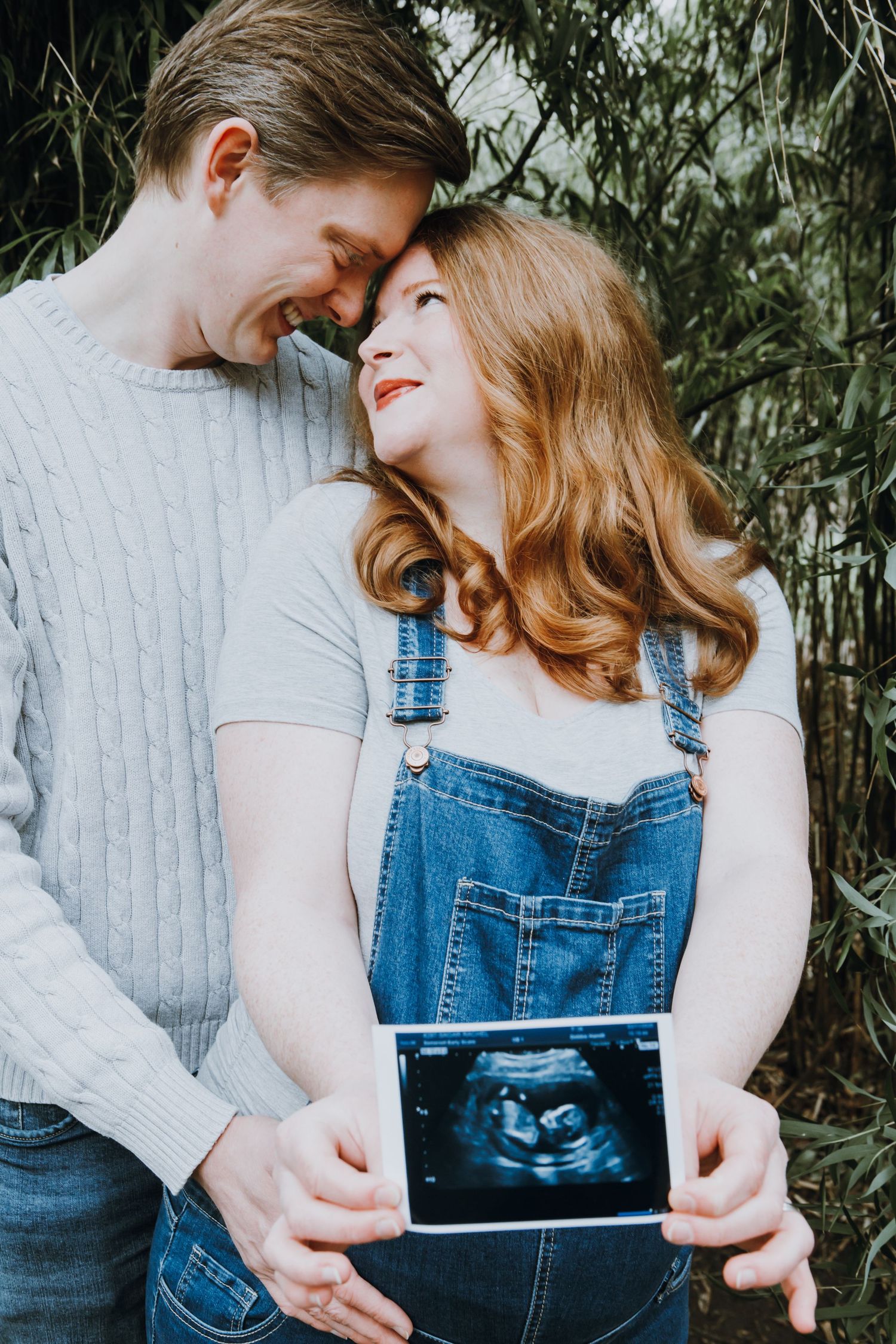 Expectant couple embracing outdoors while holding an ultrasound scan during a pregnancy announcement photoshoot.