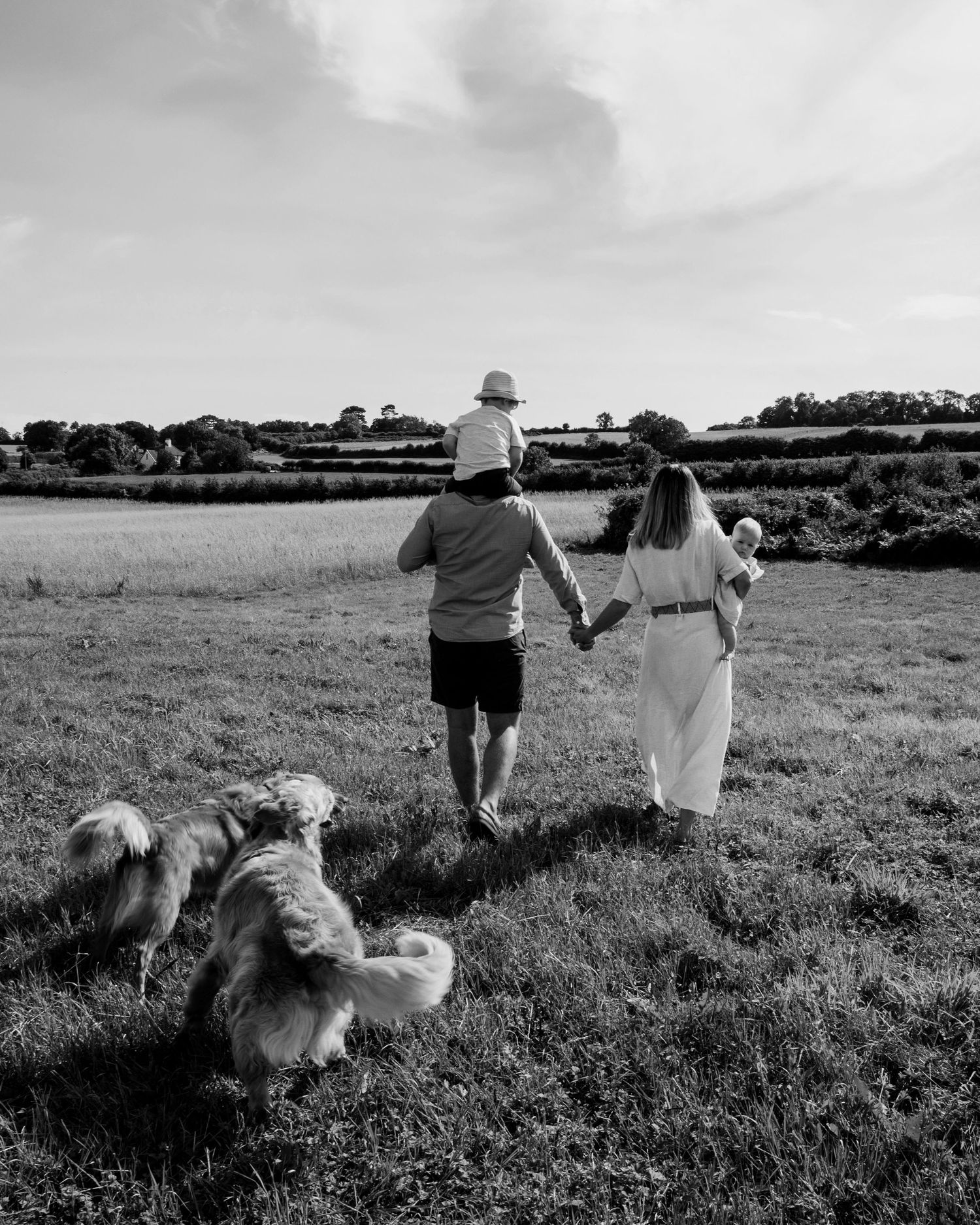 Family walking through the Somerset countryside with their children and two dogs during a relaxed outdoor family photography session.