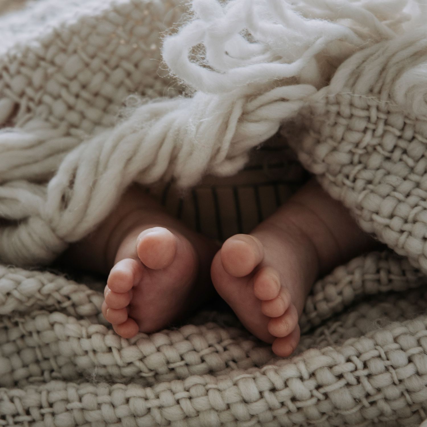 Close-up of a newborn baby's tiny feet peeking out from beneath a soft knitted blanket.