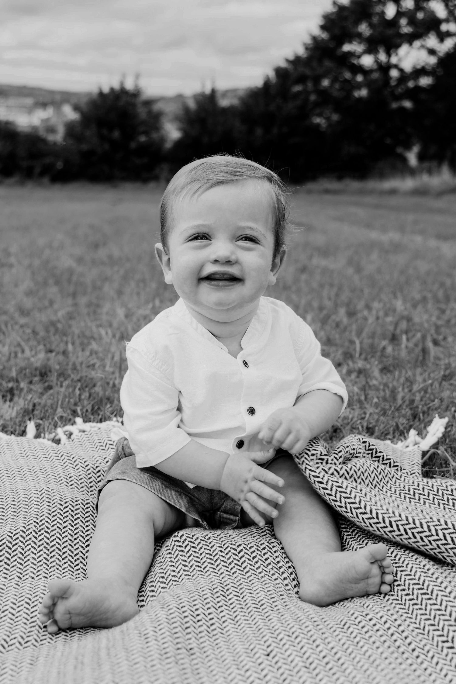 Smiling baby sitting on a woven blanket during an outdoor baby photography session in Cheltenham.