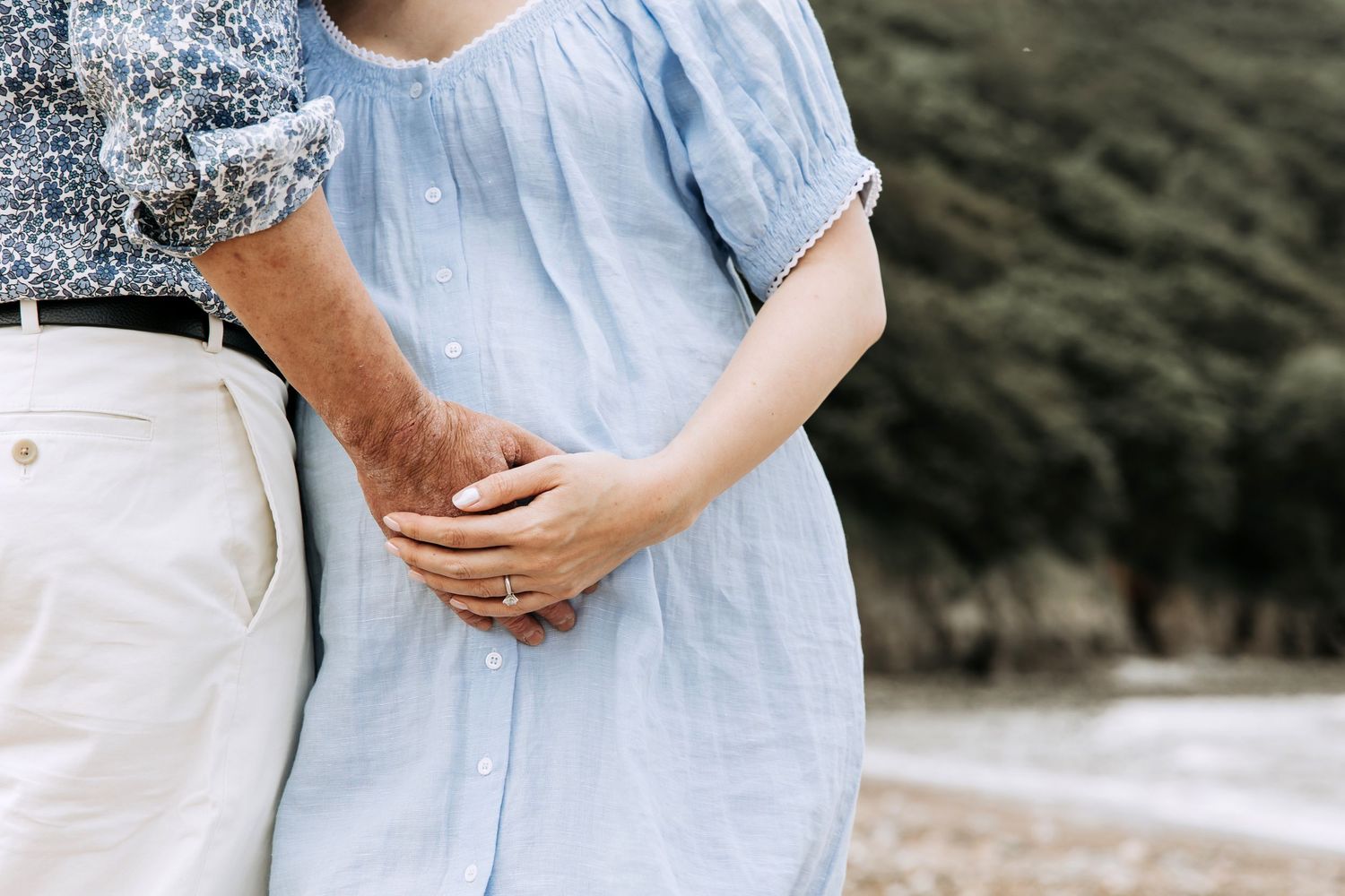 Close-up of expectant parents holding hands with one hand resting on a pregnant belly.