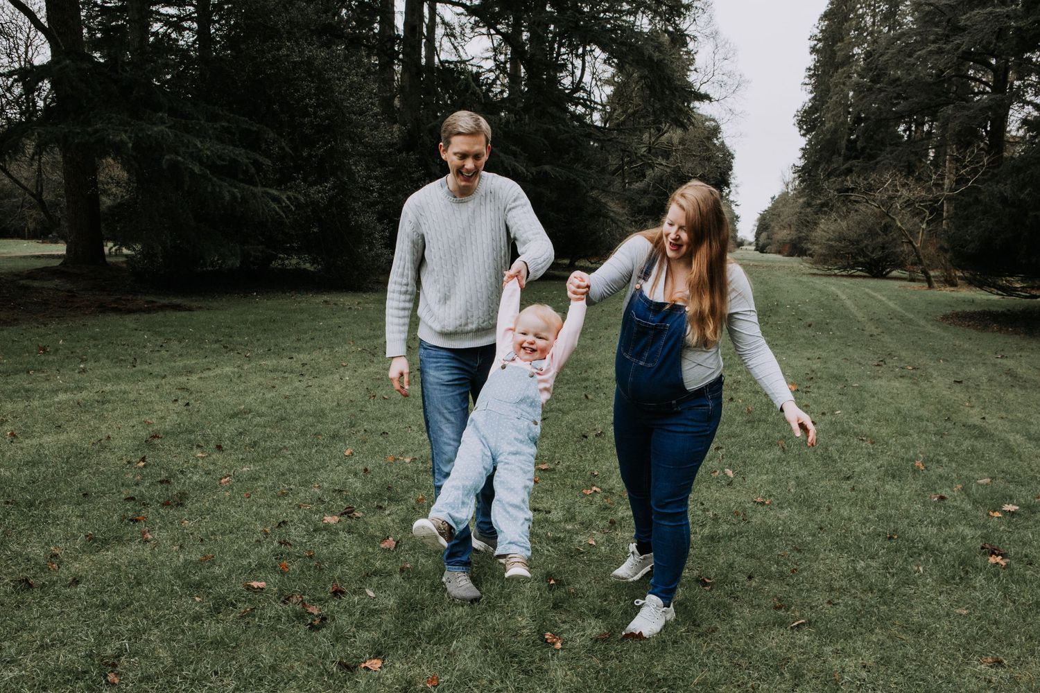 Expectant parents playing with their toddler during an outdoor family maternity photography session.