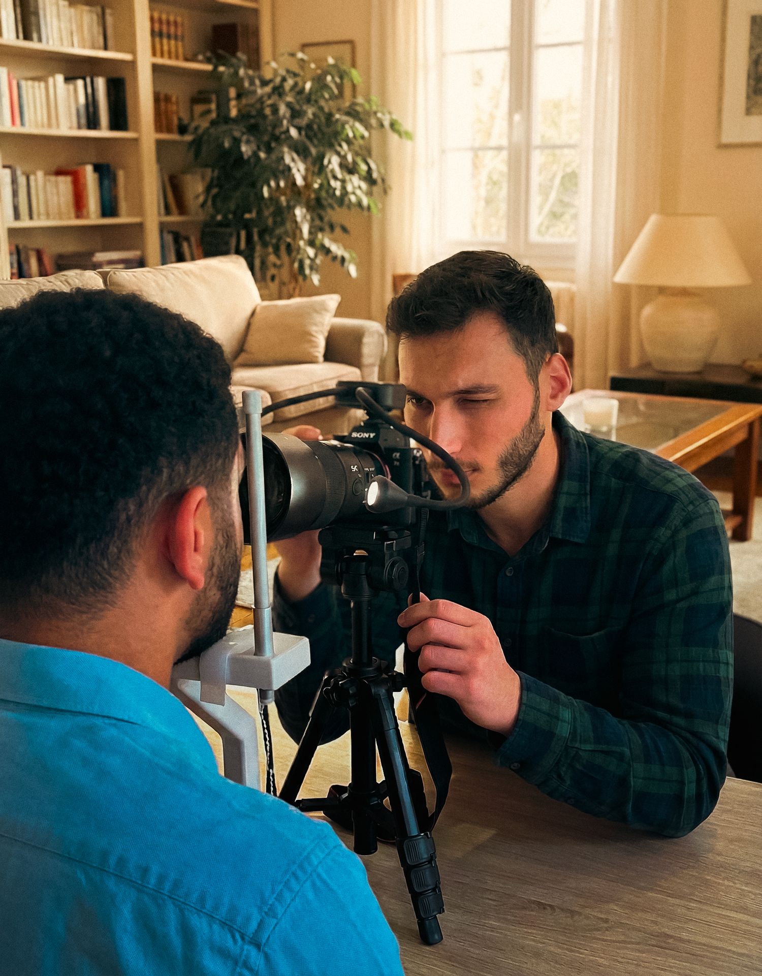 Two photographers face each other taking pictures with professional cameras in a bright room with bookshelves.