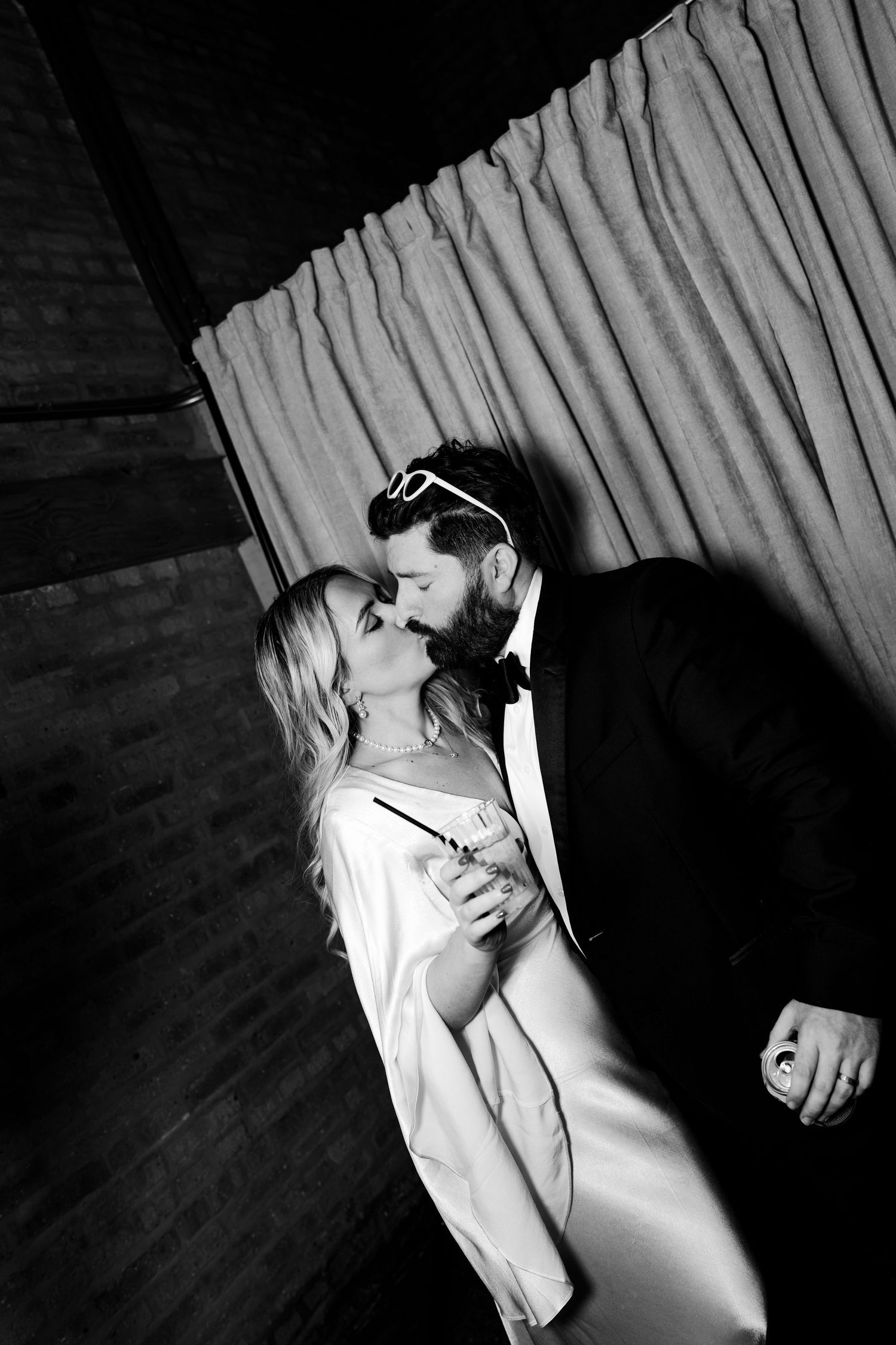 Black and white photo of a couple kissing, bride in white gown and groom in tuxedo, at an elegant wedding reception.
