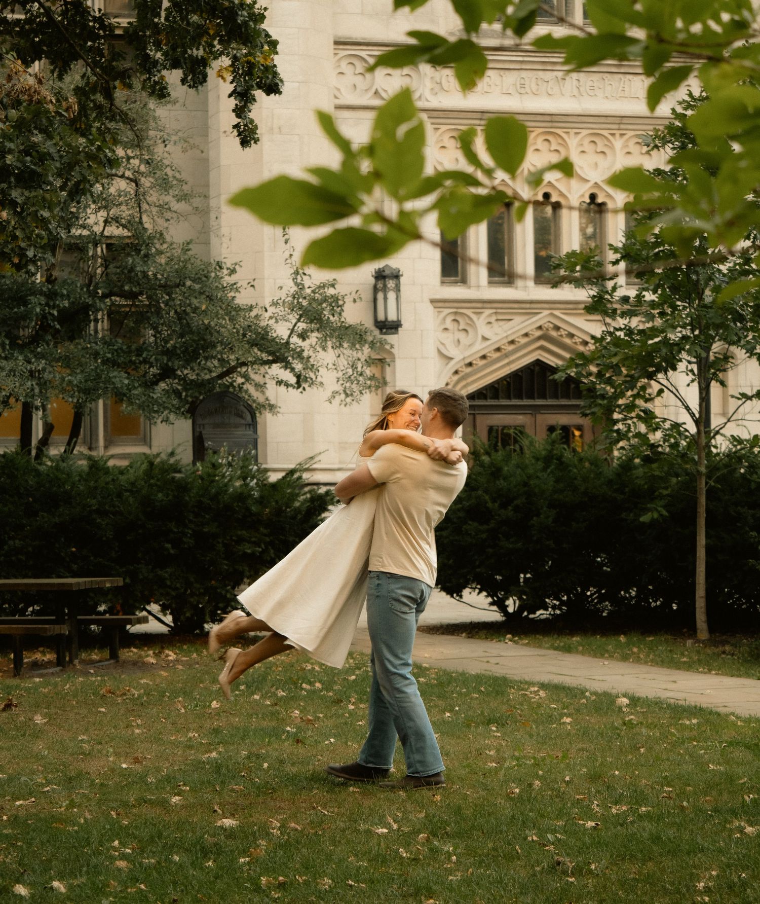 A romantic embrace on a grassy lawn with a grand architectural building visible in the background.