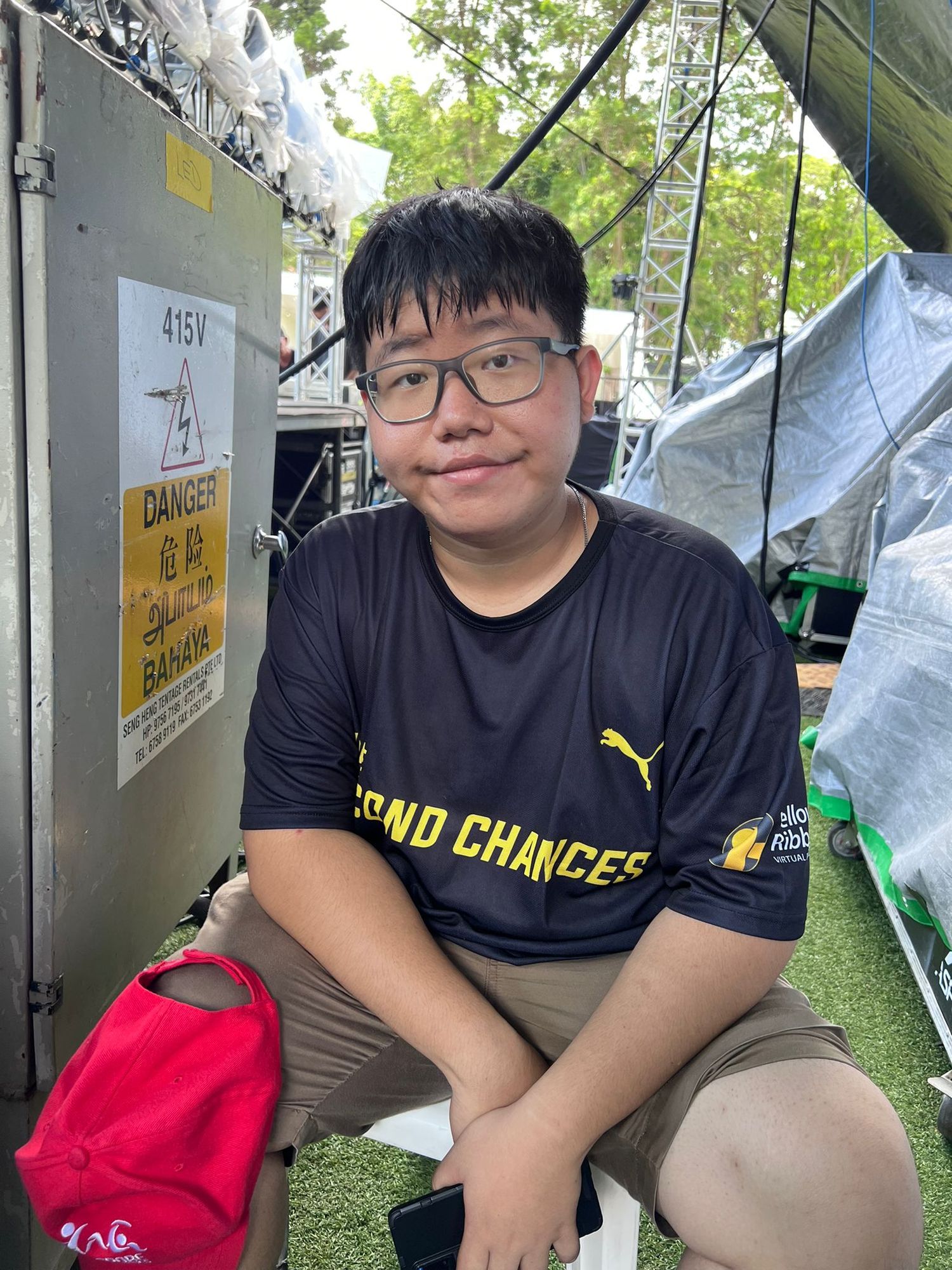 A person wearing a black Puma t-shirt with 'SEND CHANCES' text sits outdoors with a red bag nearby.
