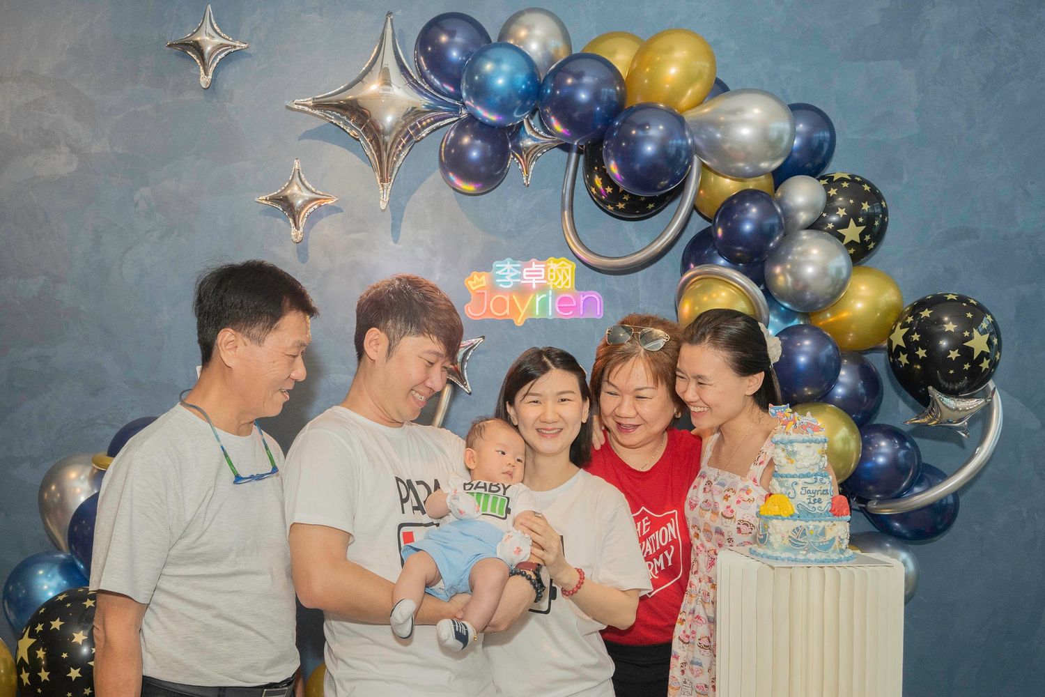 A group celebrates at a festive party with blue and gold balloons decorating the background.