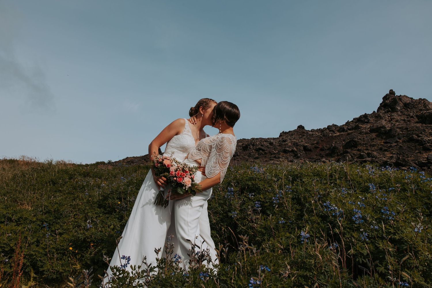 A couple embraces on a rocky cliff overlooking a dramatic mountain landscape during their wedding shoot.