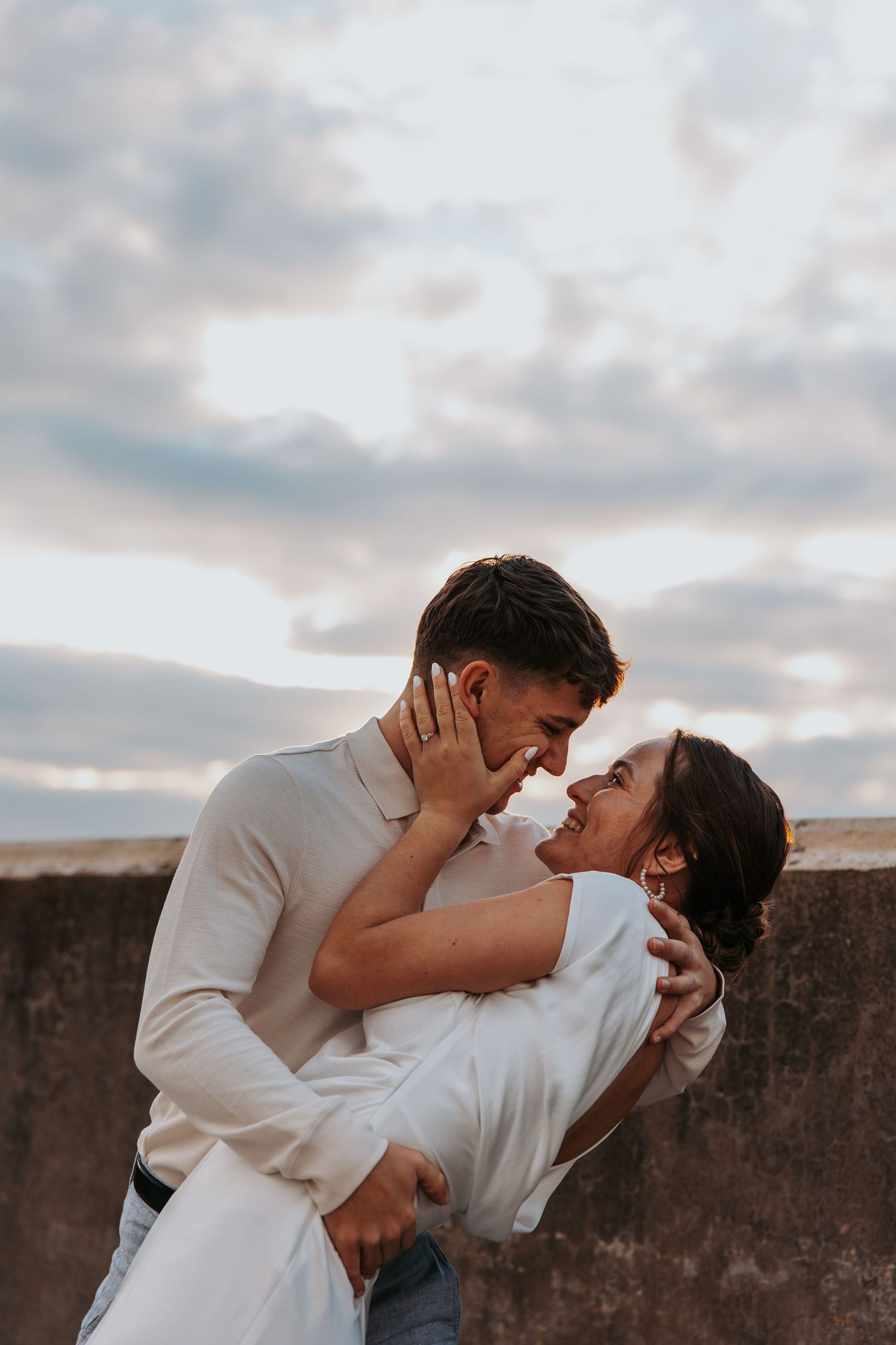 Romantic couple shares a tender moment against a cloudy sunset sky.