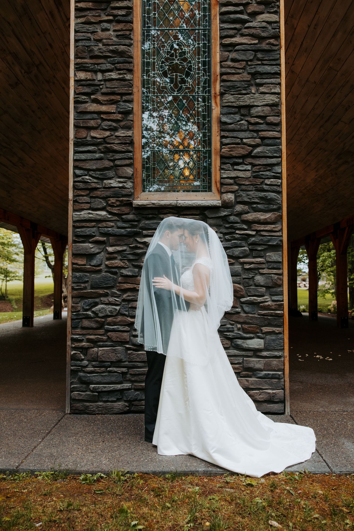 Ethereal wedding dress flowing in the breeze against a rustic stone wall chapel exterior.