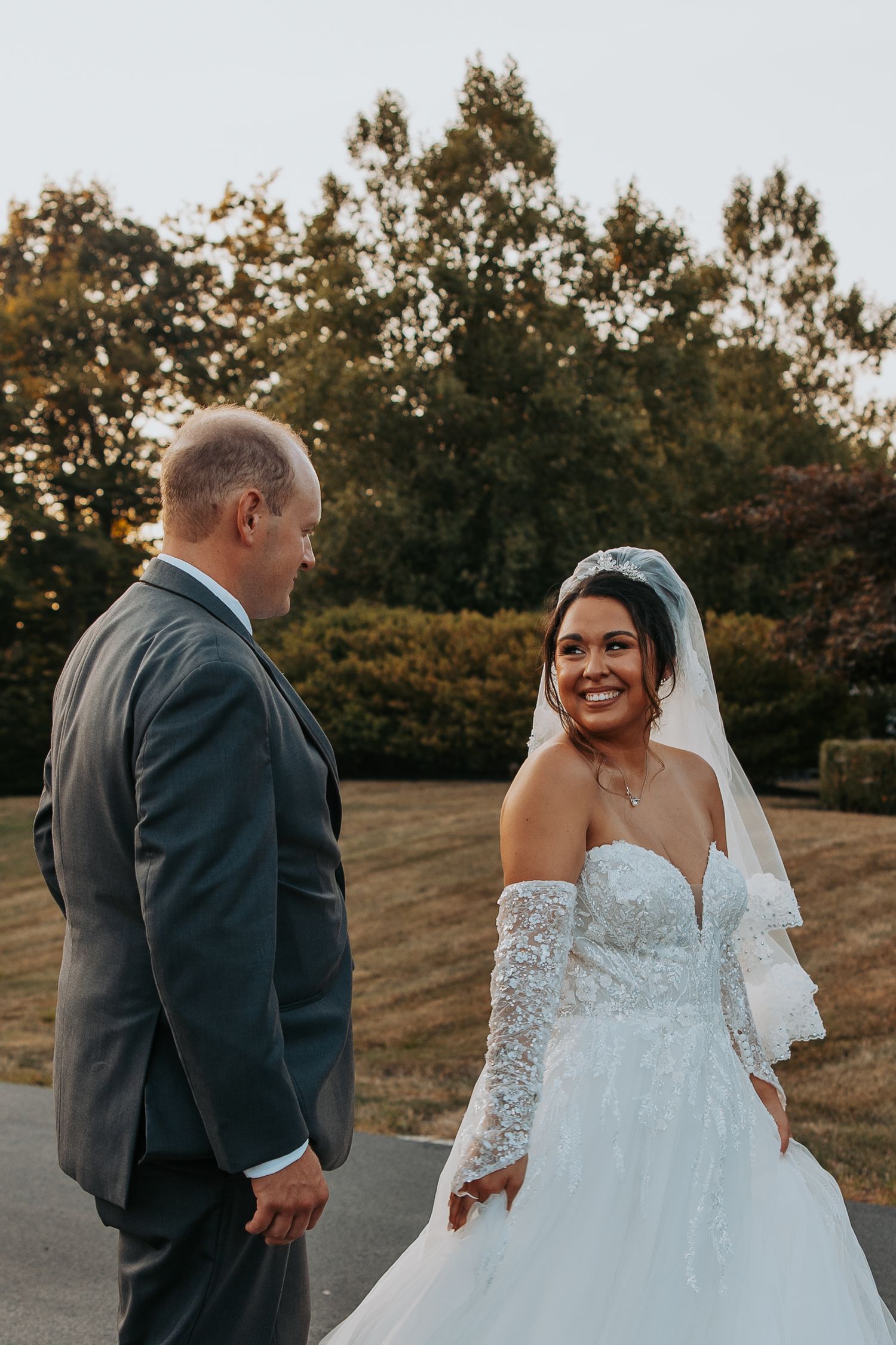 Newlyweds in elegant attire share candid moments during outdoor autumn photoshoot.