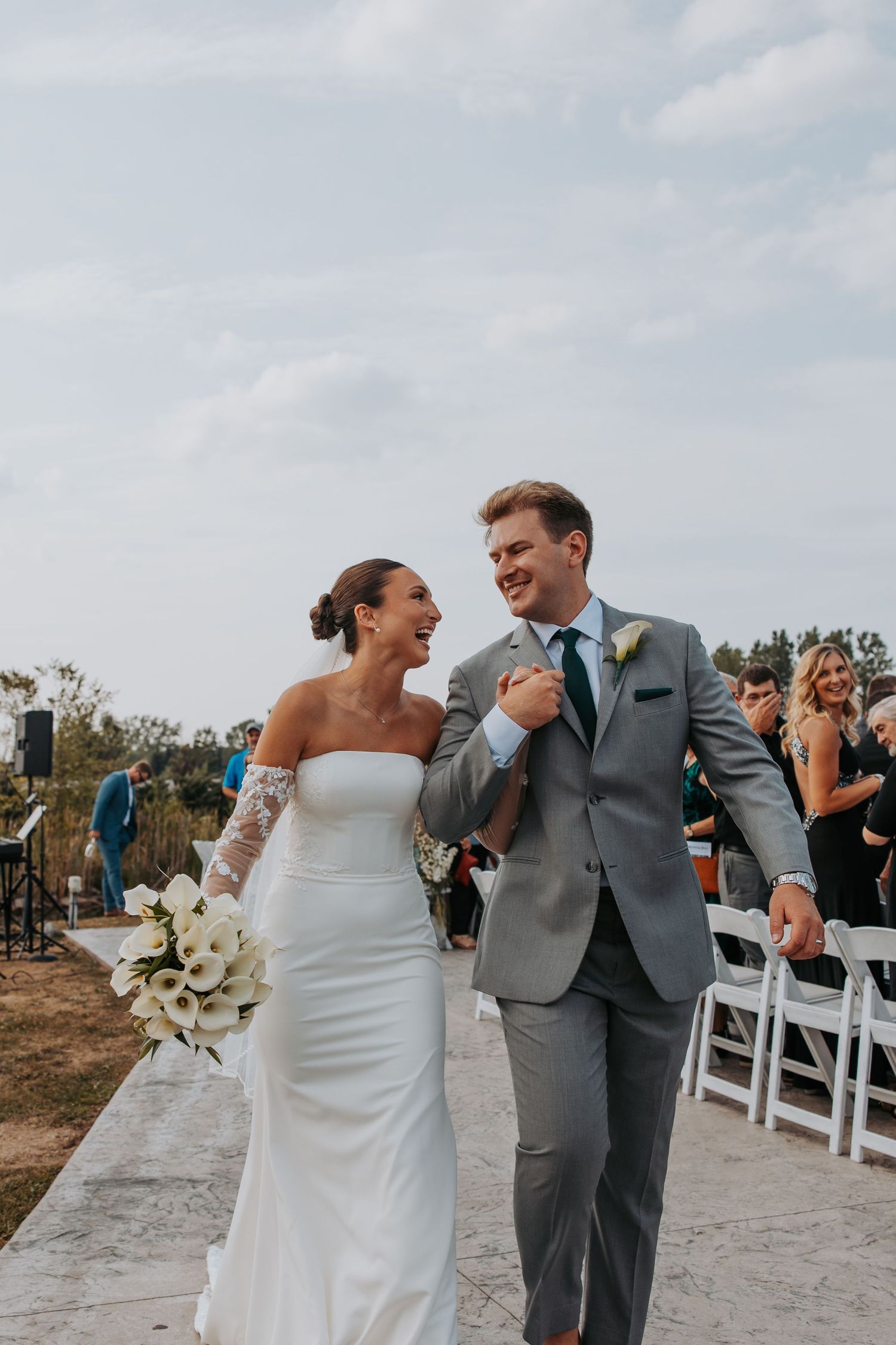 Joyful couple celebrates during beach wedding ceremony with guests and white chairs.