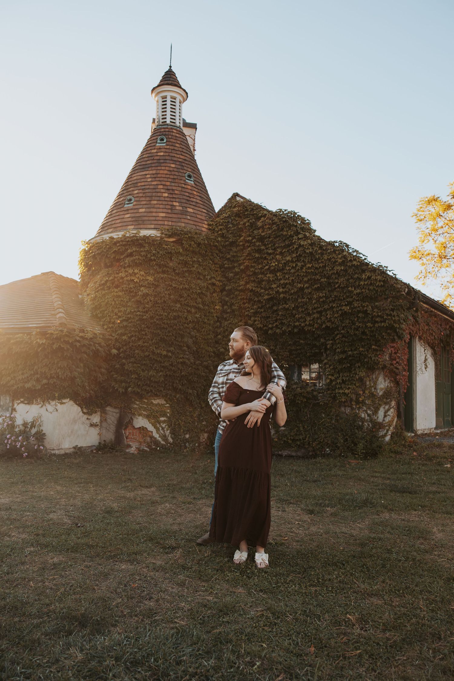 A silhouette stands in front of a rustic stone building with a conical tower at sunset.