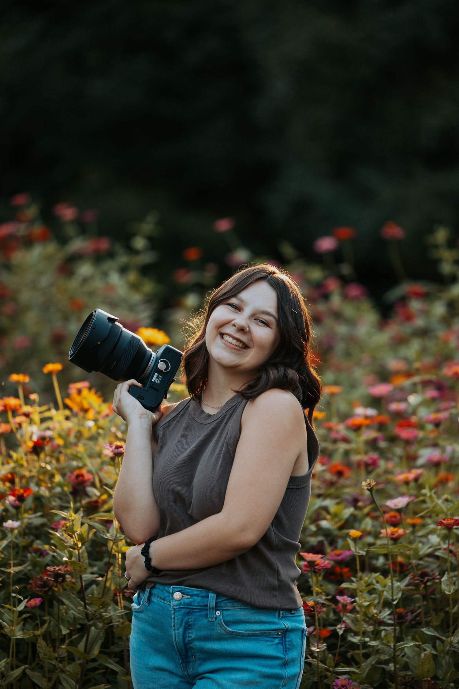 A photographer poses with a camera in a vibrant garden of orange and red zinnias on a summer day.