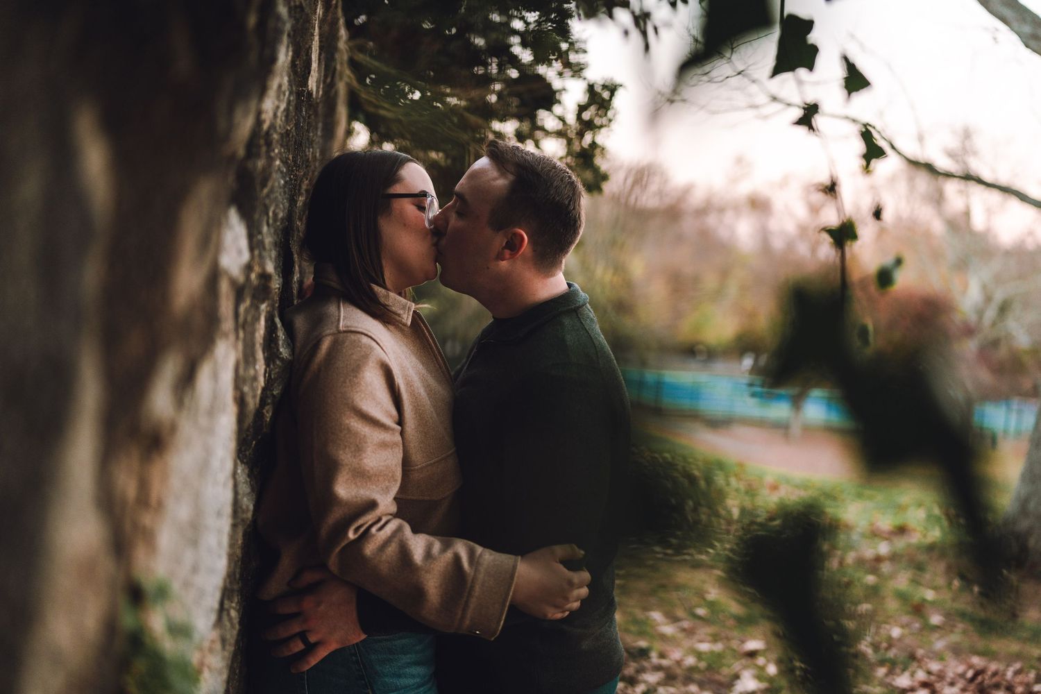 A romantic couple embracing outdoors in a park during autumn with soft bokeh lighting effects in the background.