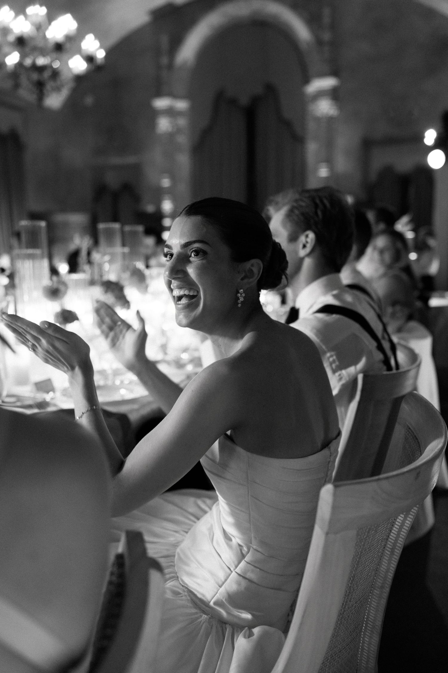 Bride in strapless gown laughs joyfully during wedding reception in ornate candlelit venue.