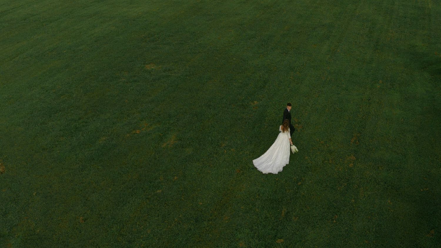 A white wedding dress hangs suspended in front of a lush green lawn background.