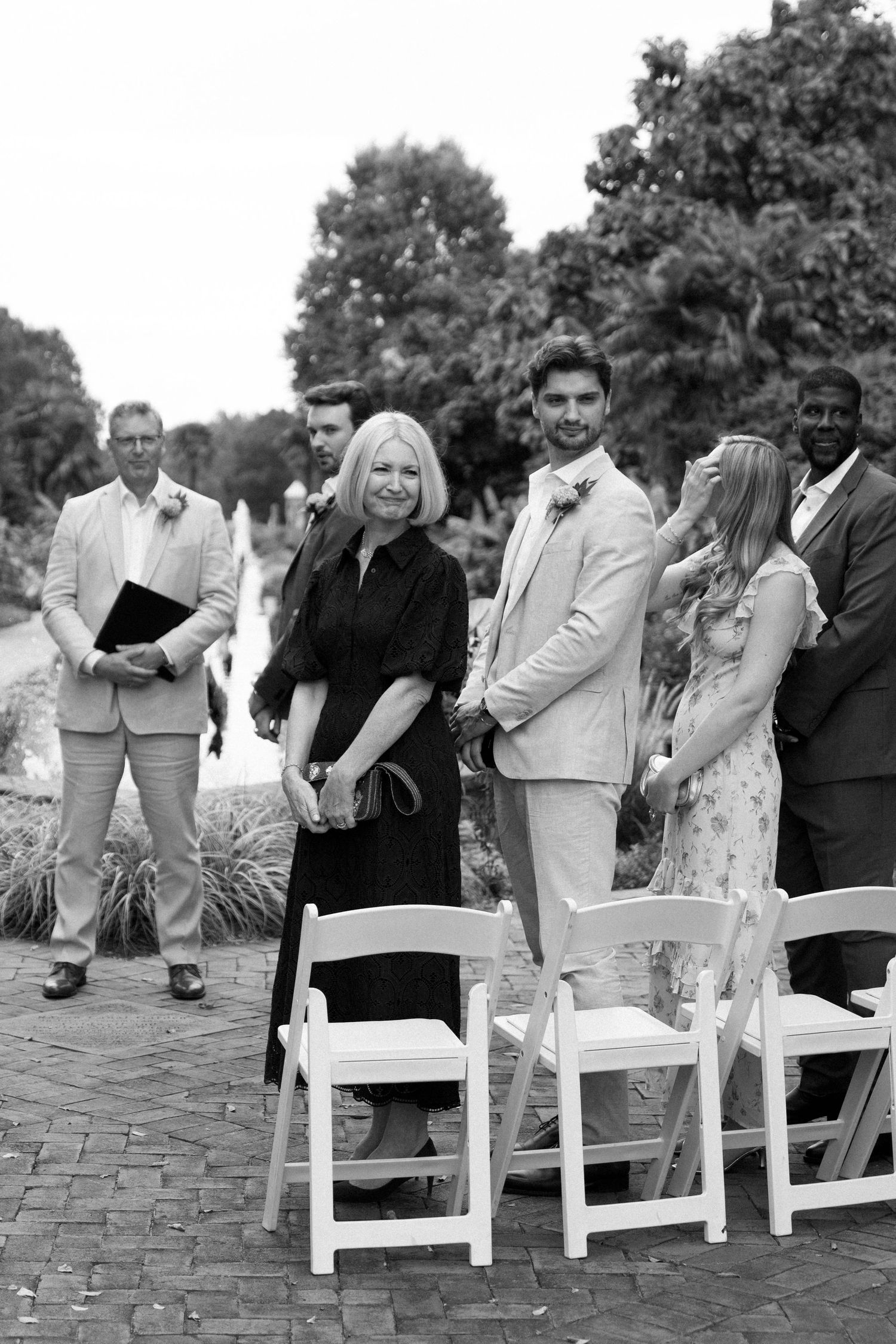 A sequence of black and white photos showing couples kissing in white chairs at an outdoor wedding ceremony.
