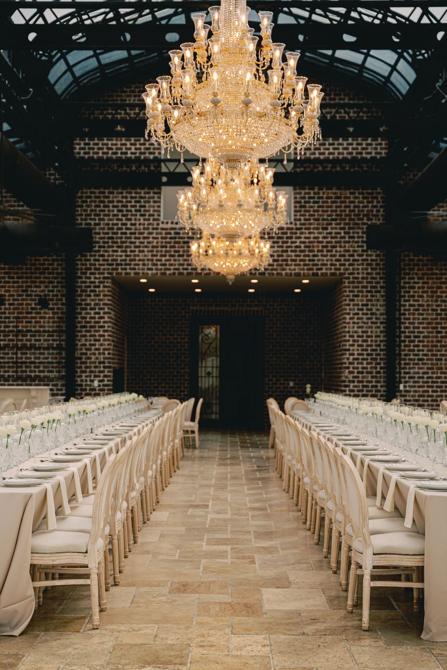 Elegant reception hall with grand crystal chandelier and rows of white chairs along dining tables.