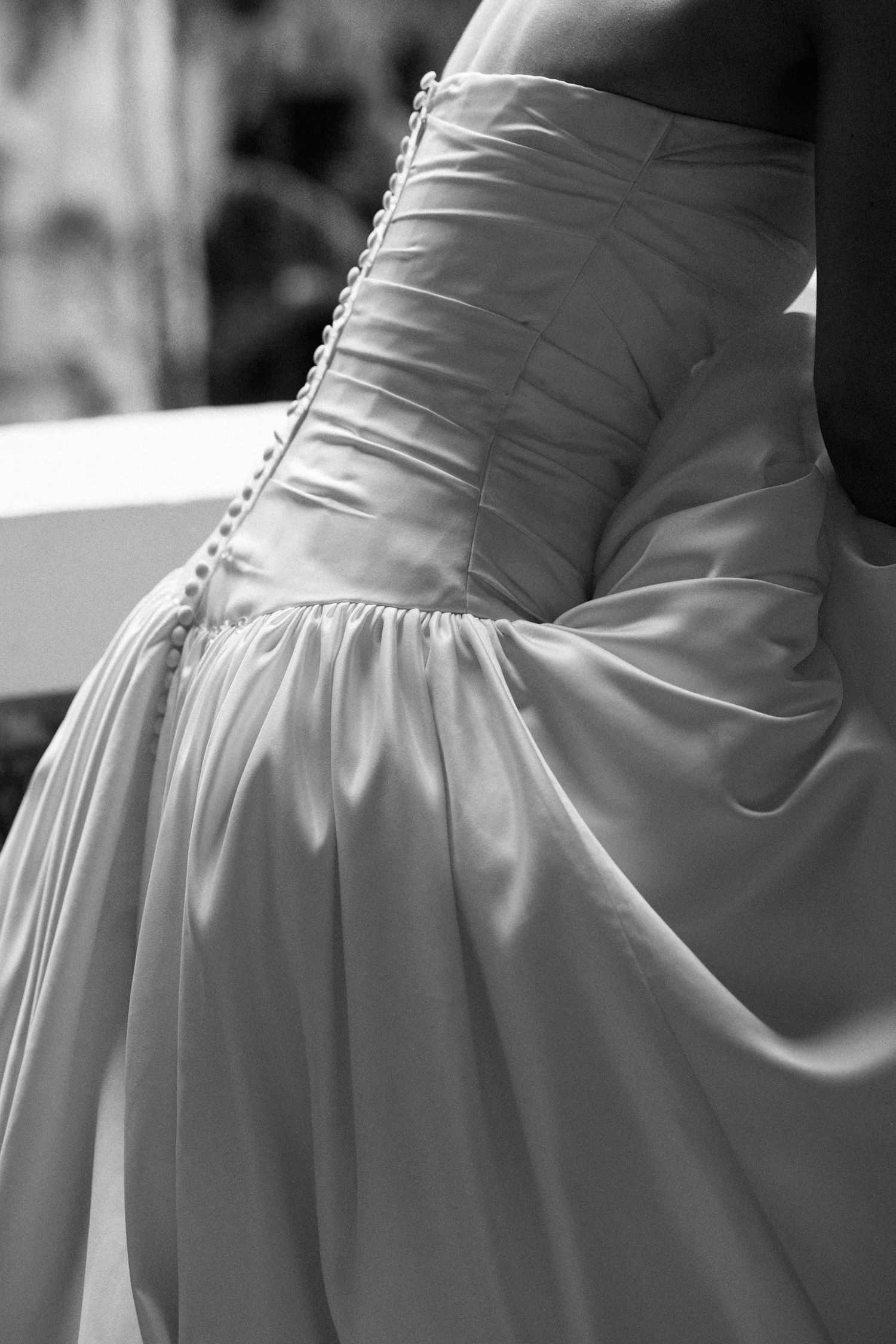 Black and white close-up of an elegant wedding dress with ruched bodice, button details, and flowing satin skirt.