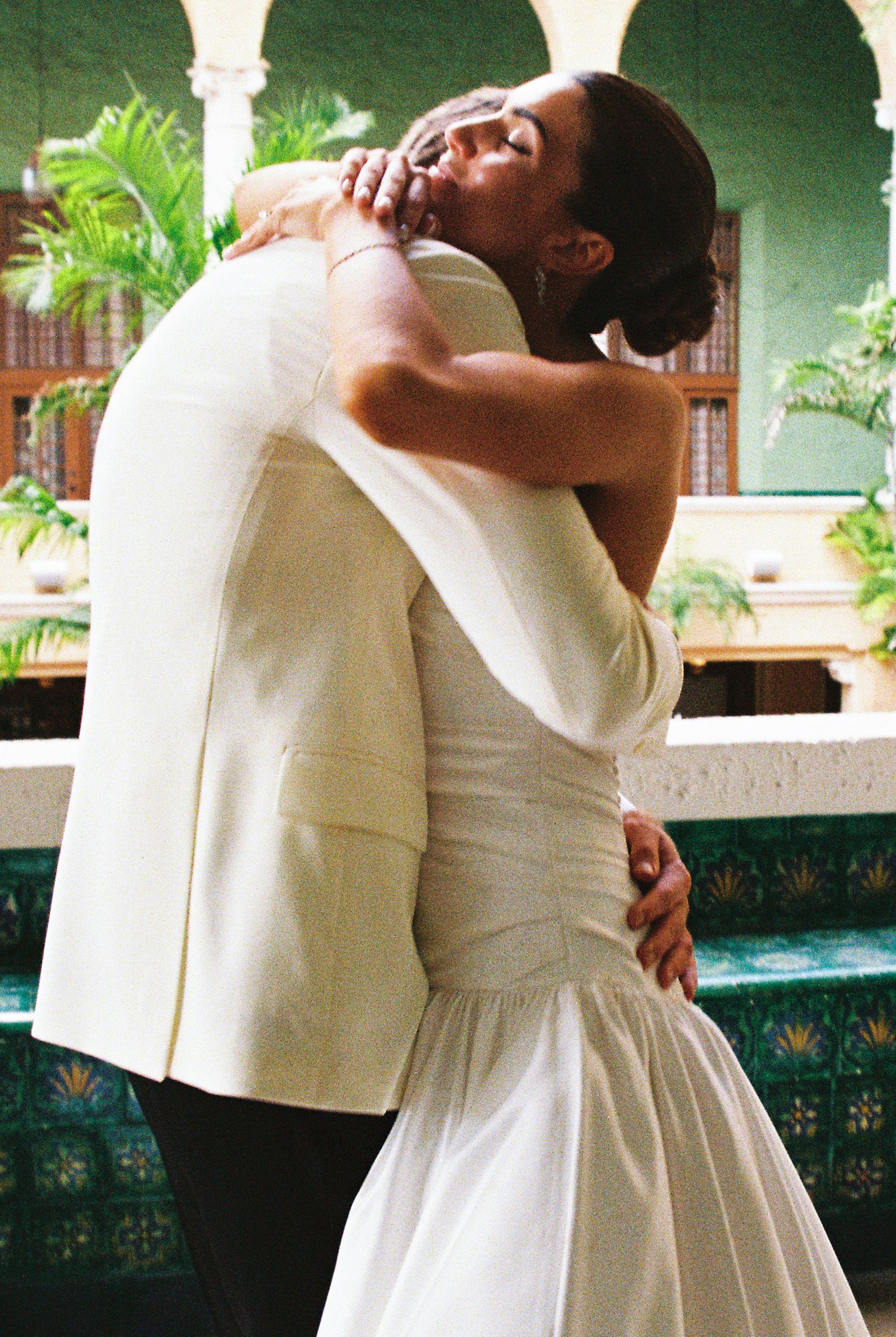 A couple in wedding attire shares a romantic embrace, with the bride in a white gown and groom in a cream suit.