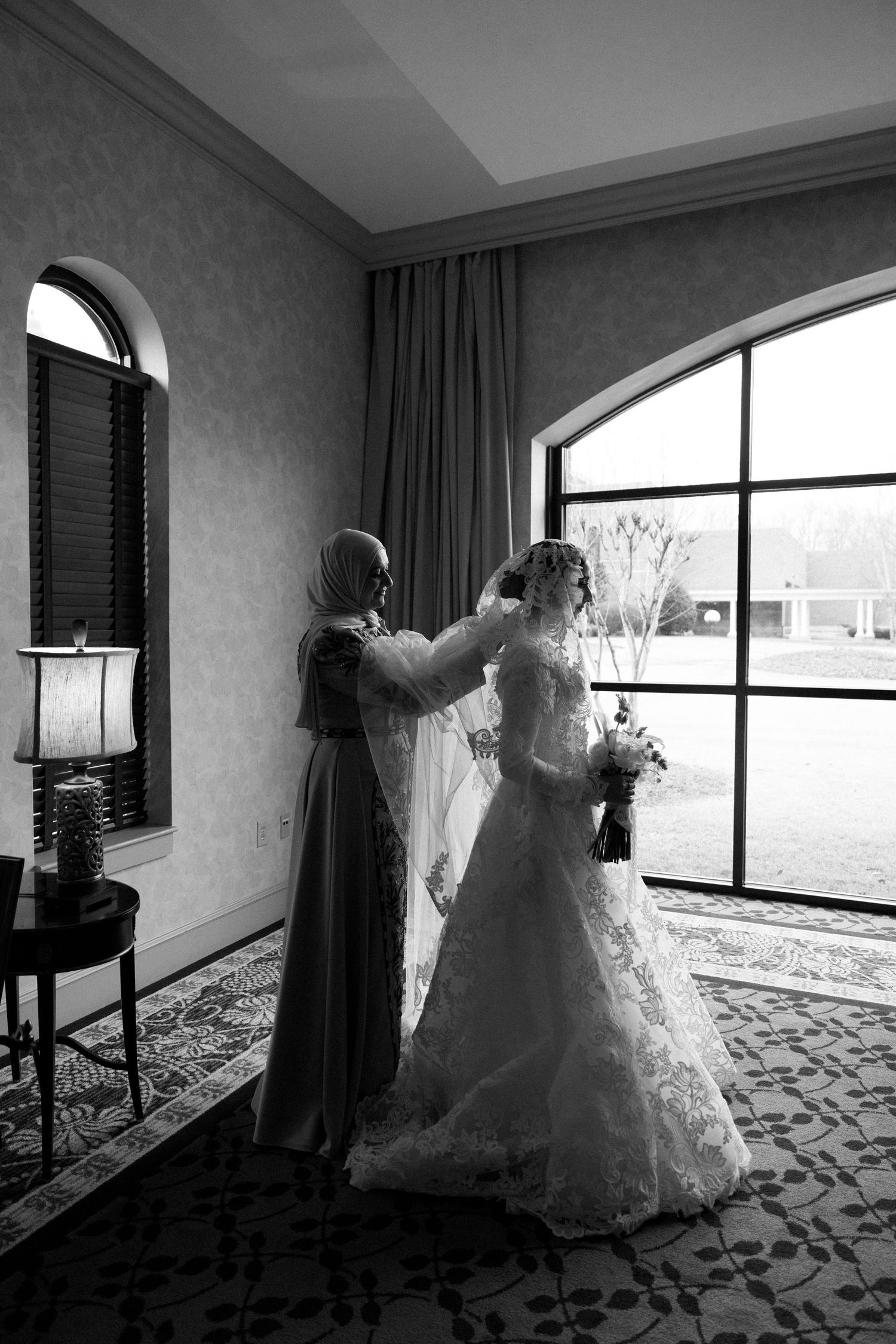 A wedding dress displayed in a room with large windows and patterned carpet, shown in a series of black and white photos.