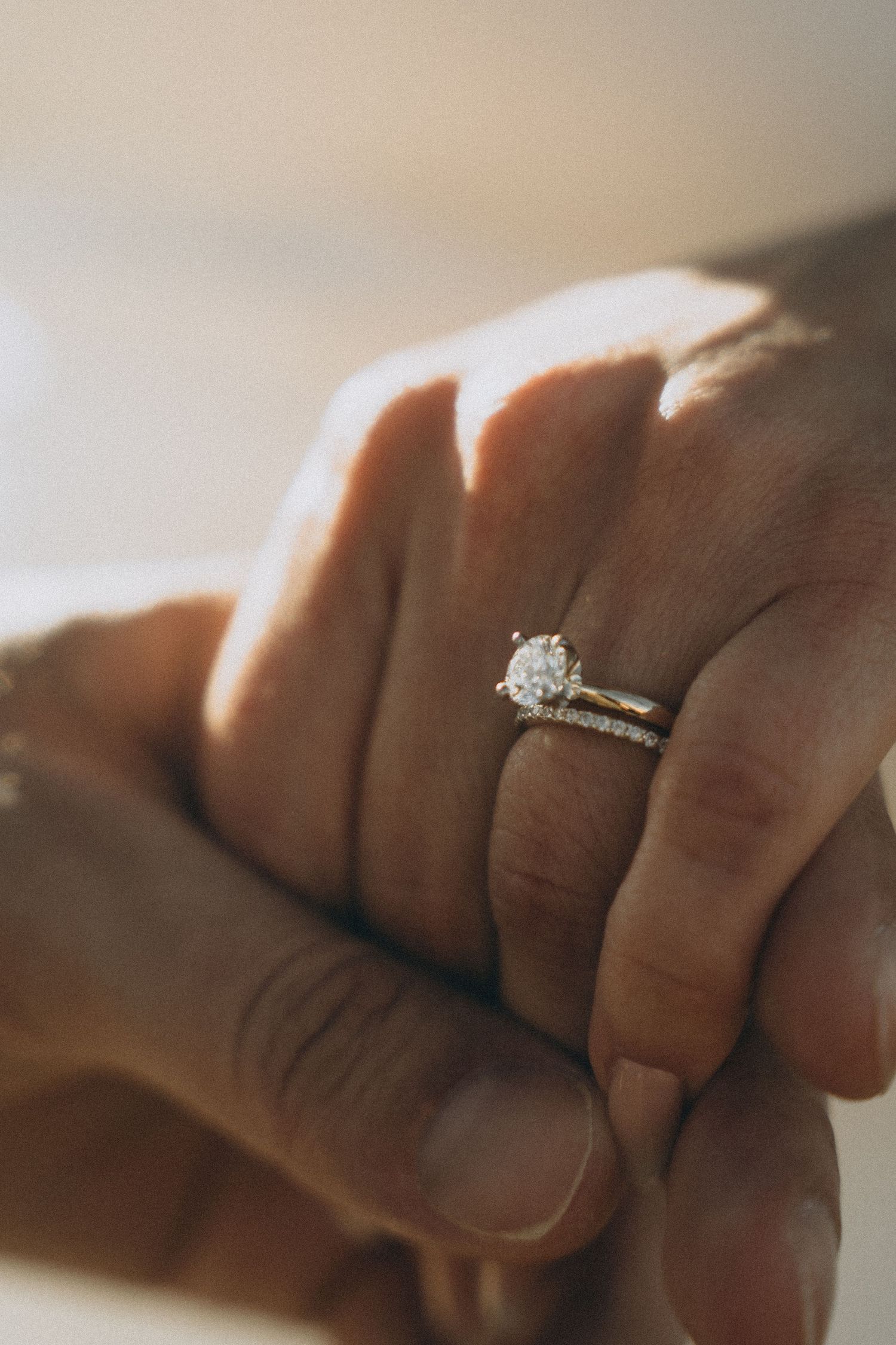 Close-up of a solitaire diamond engagement ring on hand in warm natural lighting.