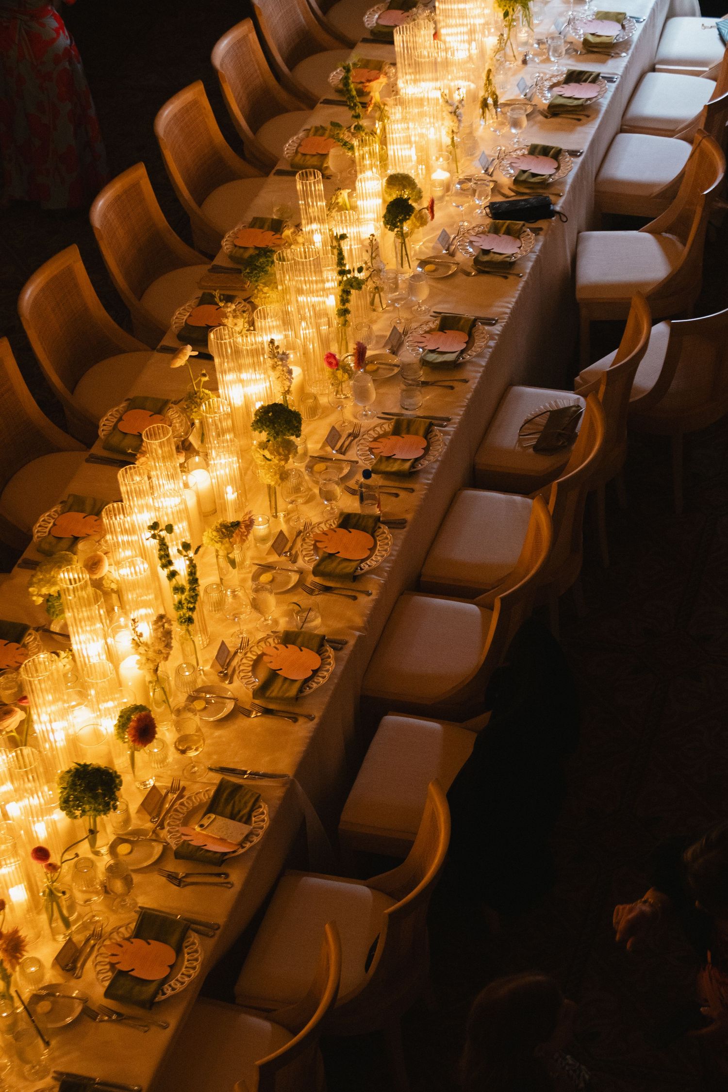 Elegantly set long reception dinner table glowing with tall crystal candle centerpieces and floral arrangements.