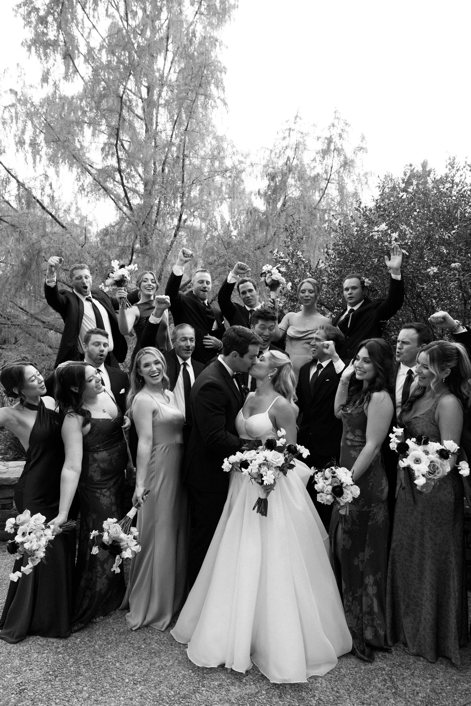A black and white photo series showing a wedding party in formal attire celebrating together outdoors.