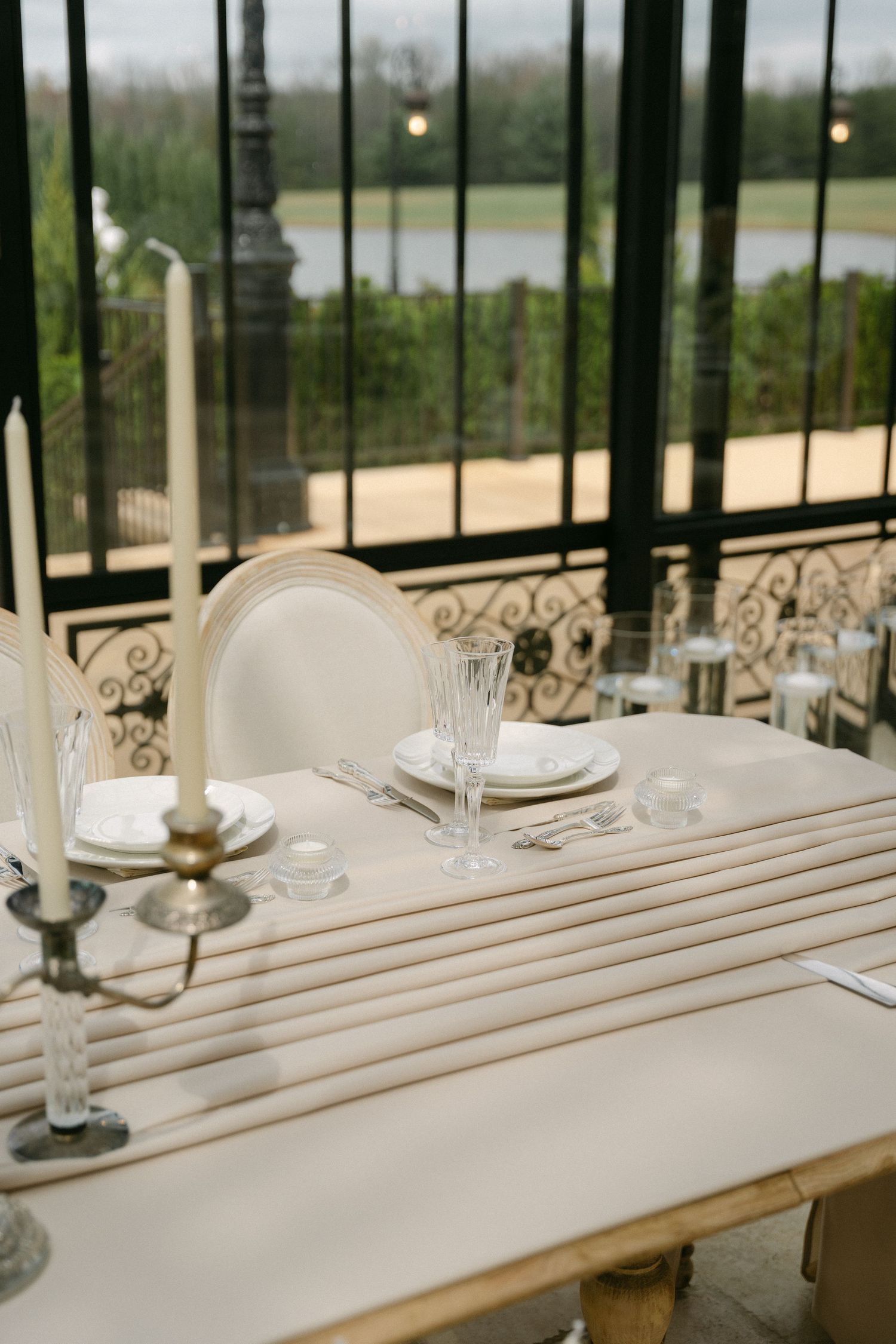 Elegant table setting at reception venue with candlesticks and white linens overlooking water view through iron railings.