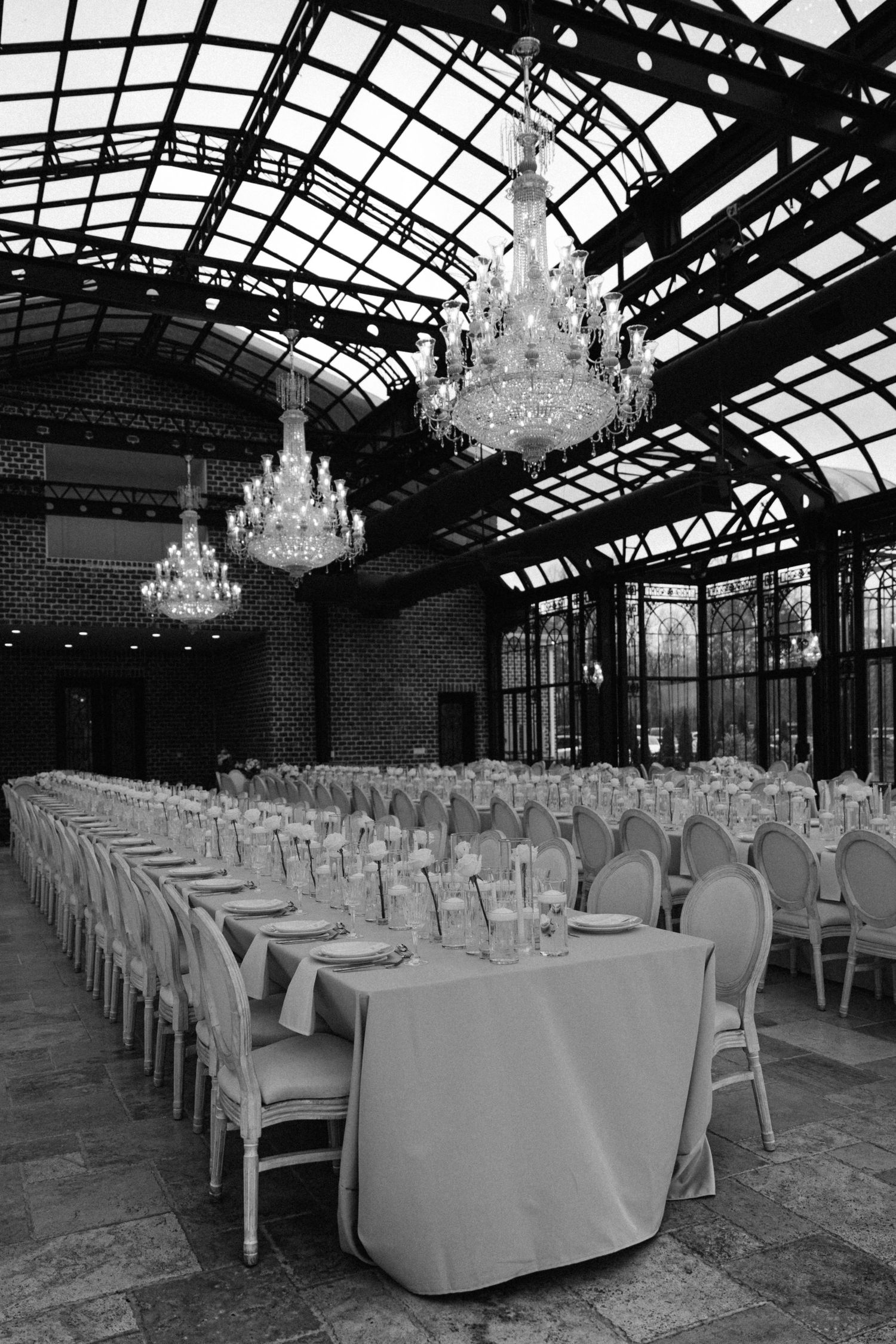 Elegant banquet hall with crystal chandeliers and long tables arranged in rows under a glass-paneled ceiling.