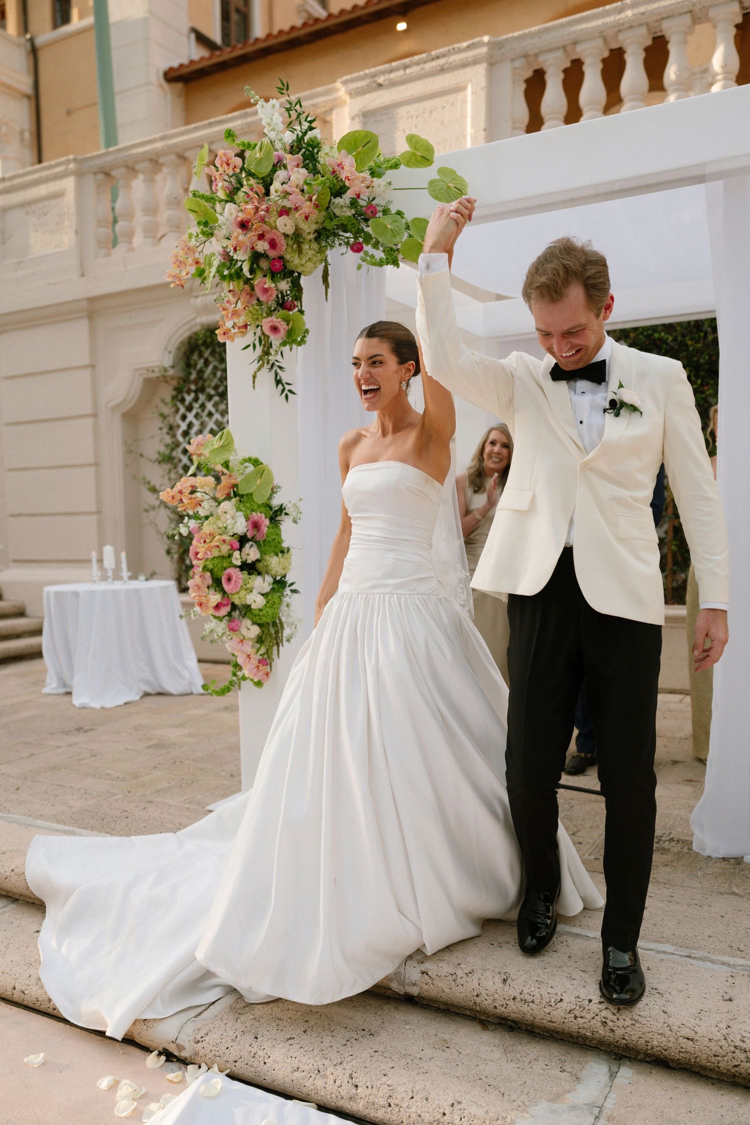 Bride and groom celebrating at outdoor wedding ceremony with pink floral arch backdrop.