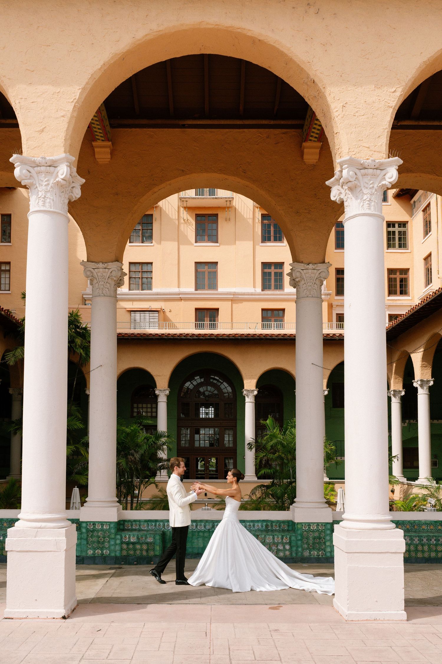 Bride and groom dancing under elegant white arched columns at a Mediterranean-style wedding venue.