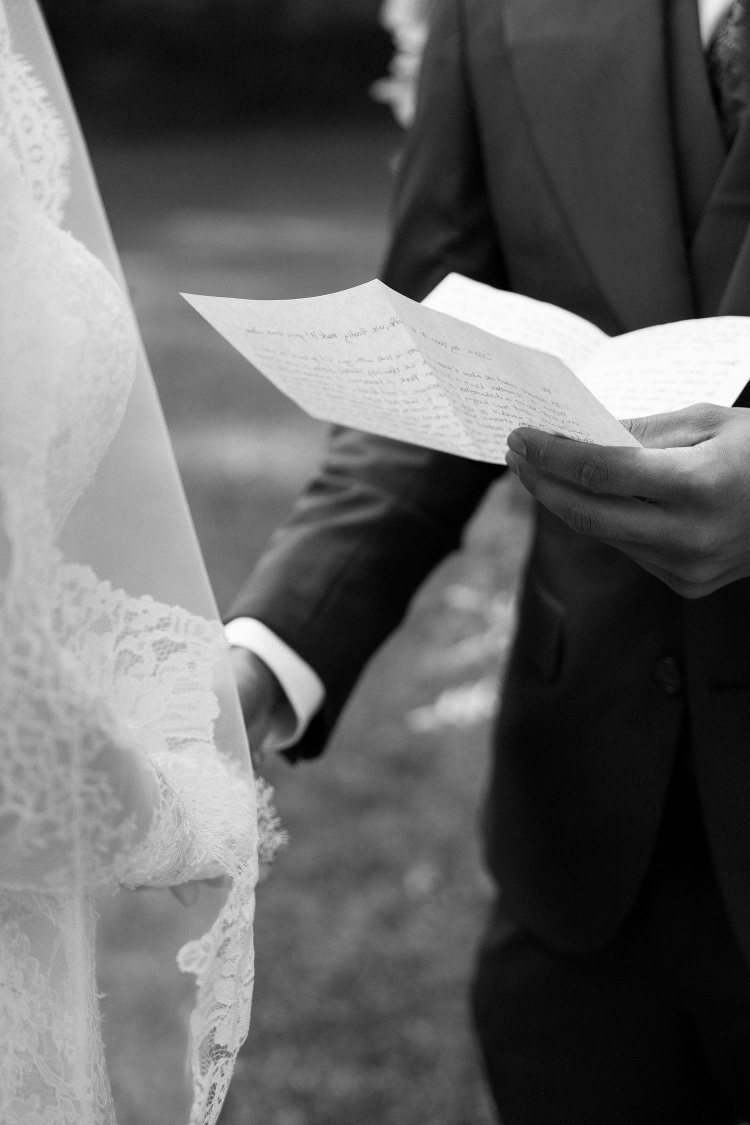 Black and white close-up of wedding ceremony participants holding papers during an outdoor service.
