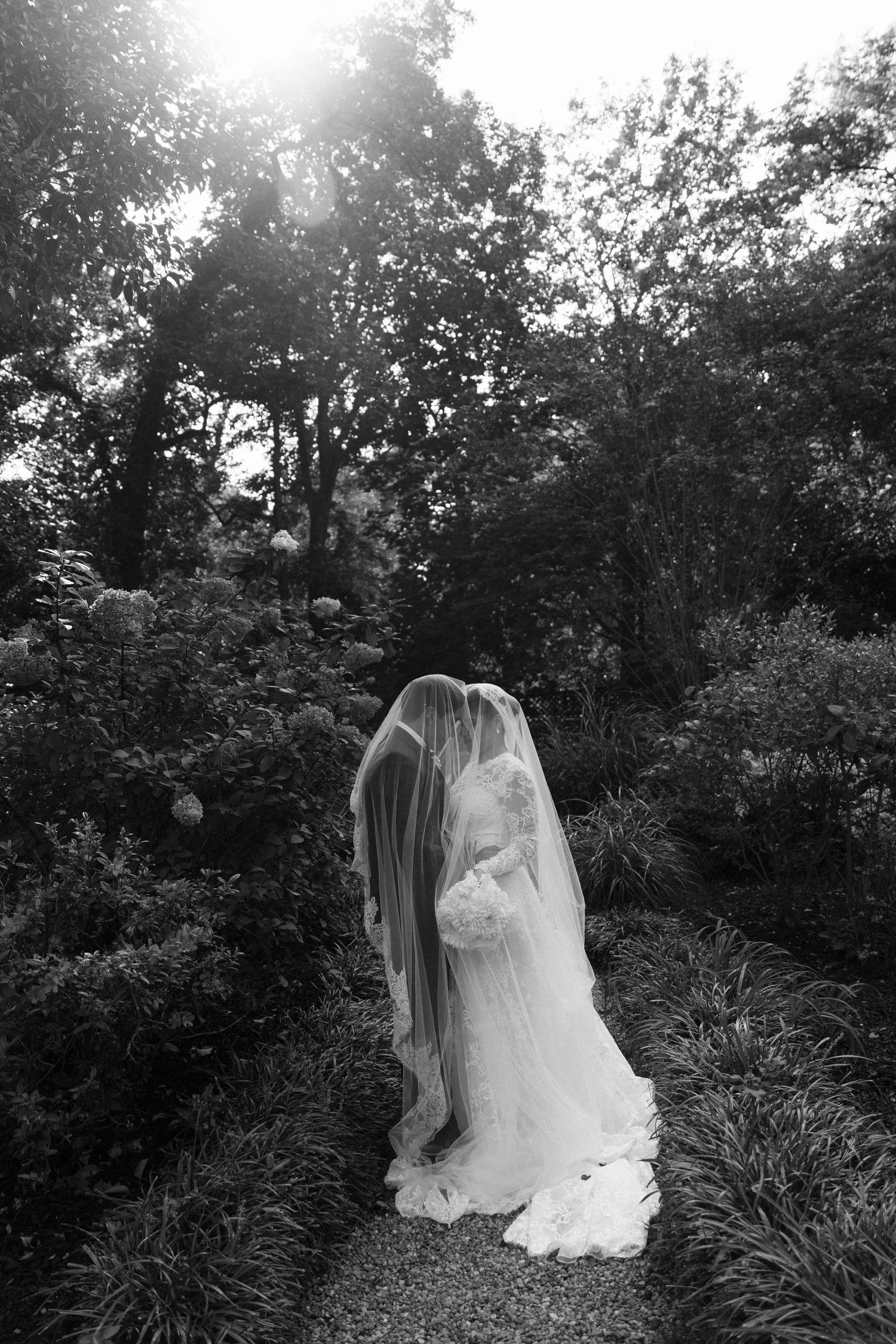 A romantic black and white garden scene with a flowing white wedding dress and veil silhouetted against lush foliage.