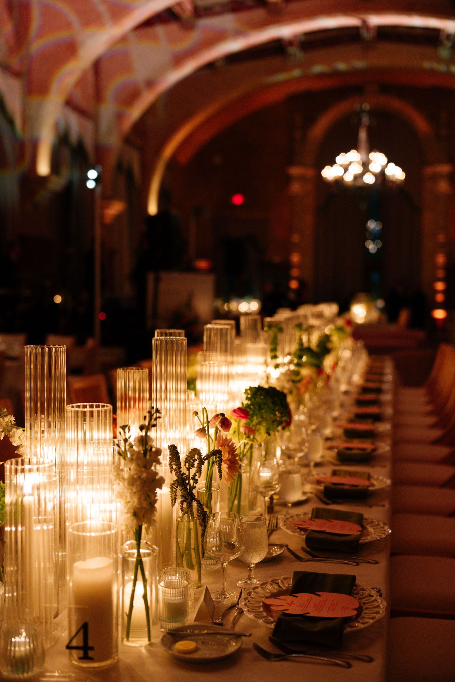 Elegant candlelit banquet table with floral centerpieces and place settings in a grand arched venue.