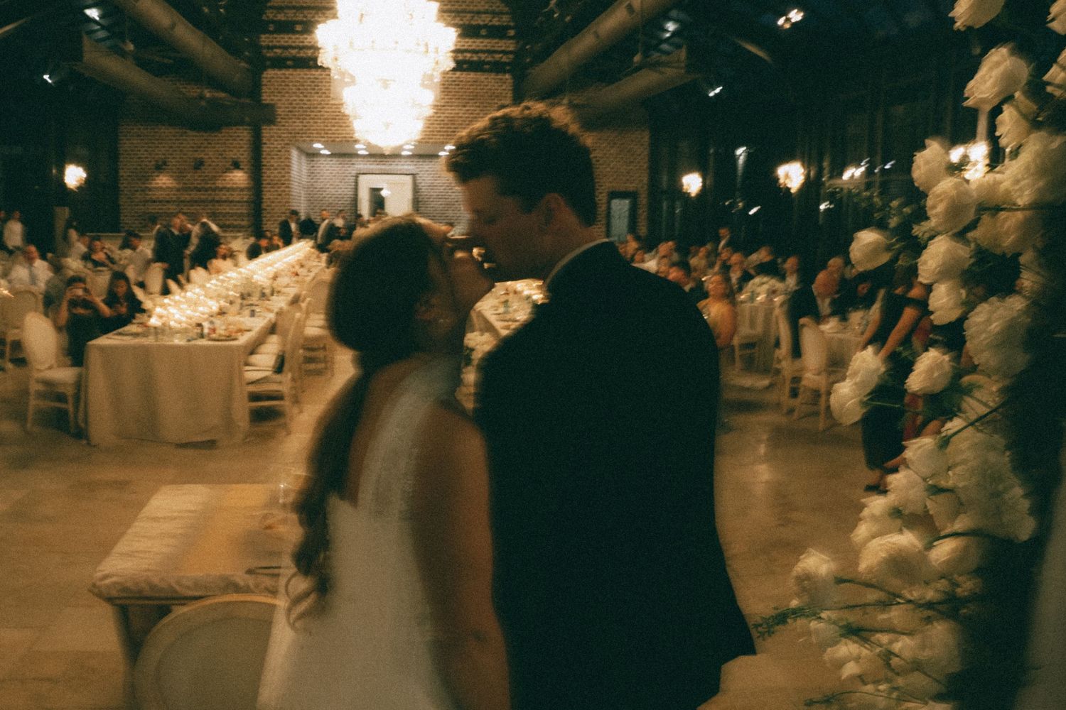 Romantic reception scene with couple dancing amid warm lighting and floral decorations.
