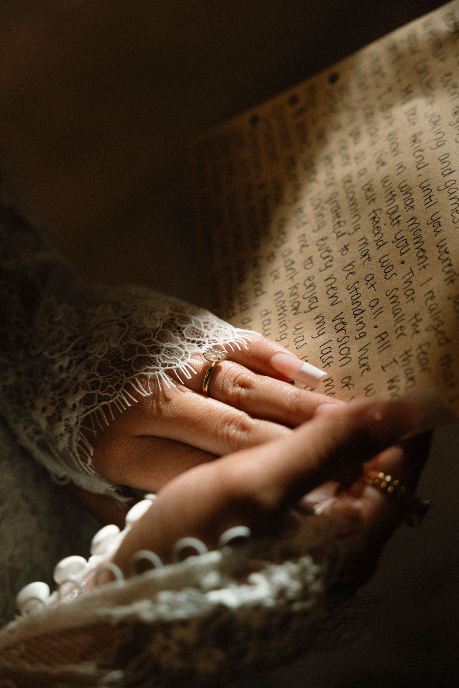 A close-up view of hands resting on an antique book page with text visible in soft lighting.