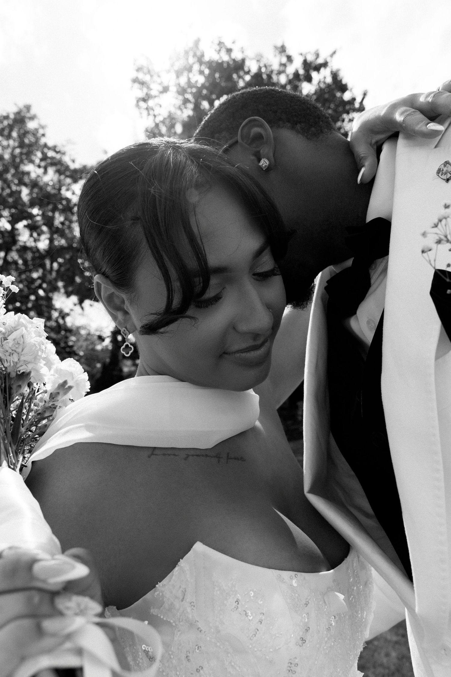 A romantic black and white photo of a couple embracing at their wedding celebration outdoors.