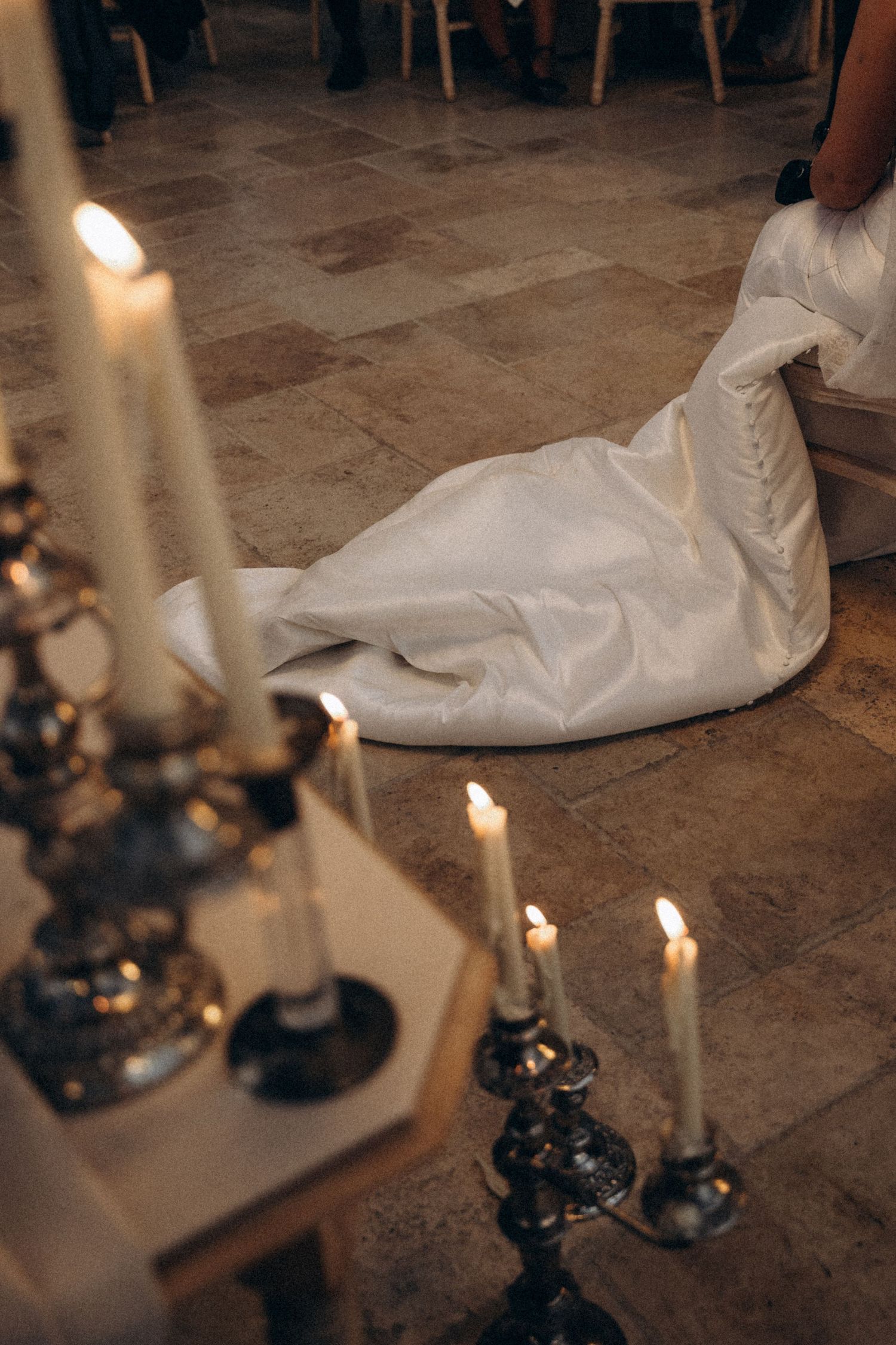 White wedding dress train lays on stone floor with glowing candles in elegant black candlesticks nearby.