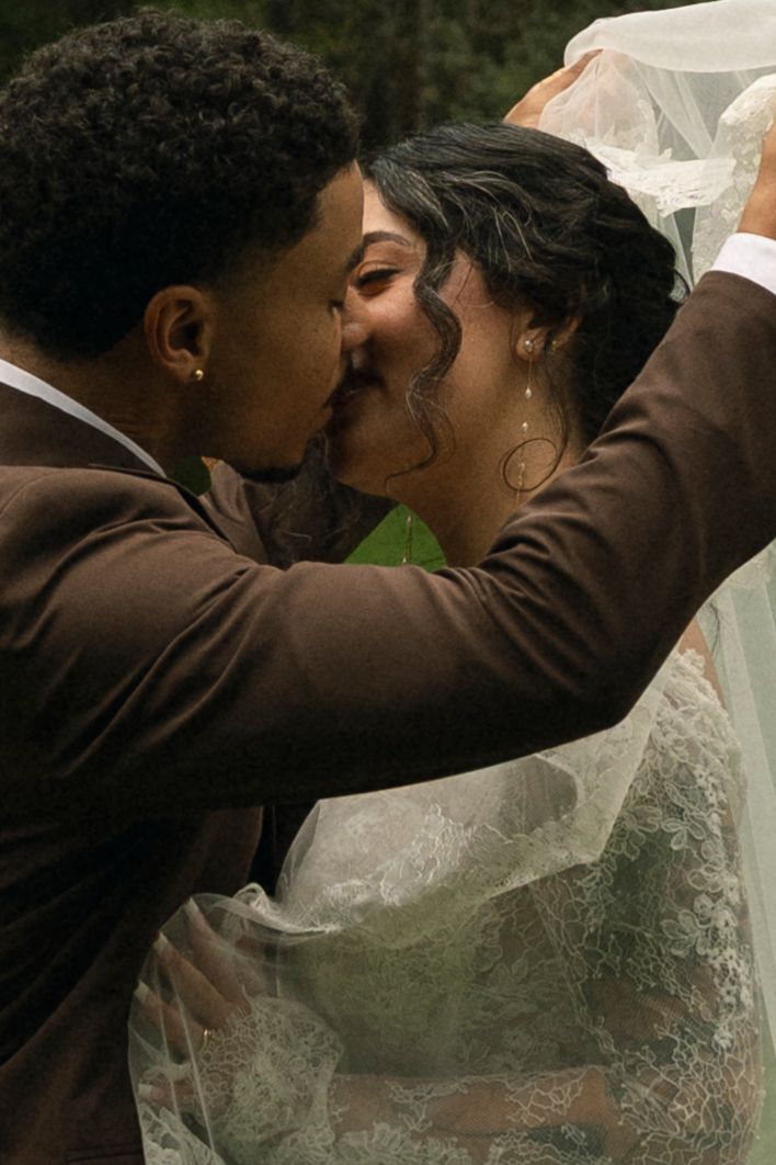 A romantic wedding kiss between a couple, with the bride's delicate veil flowing in the background.