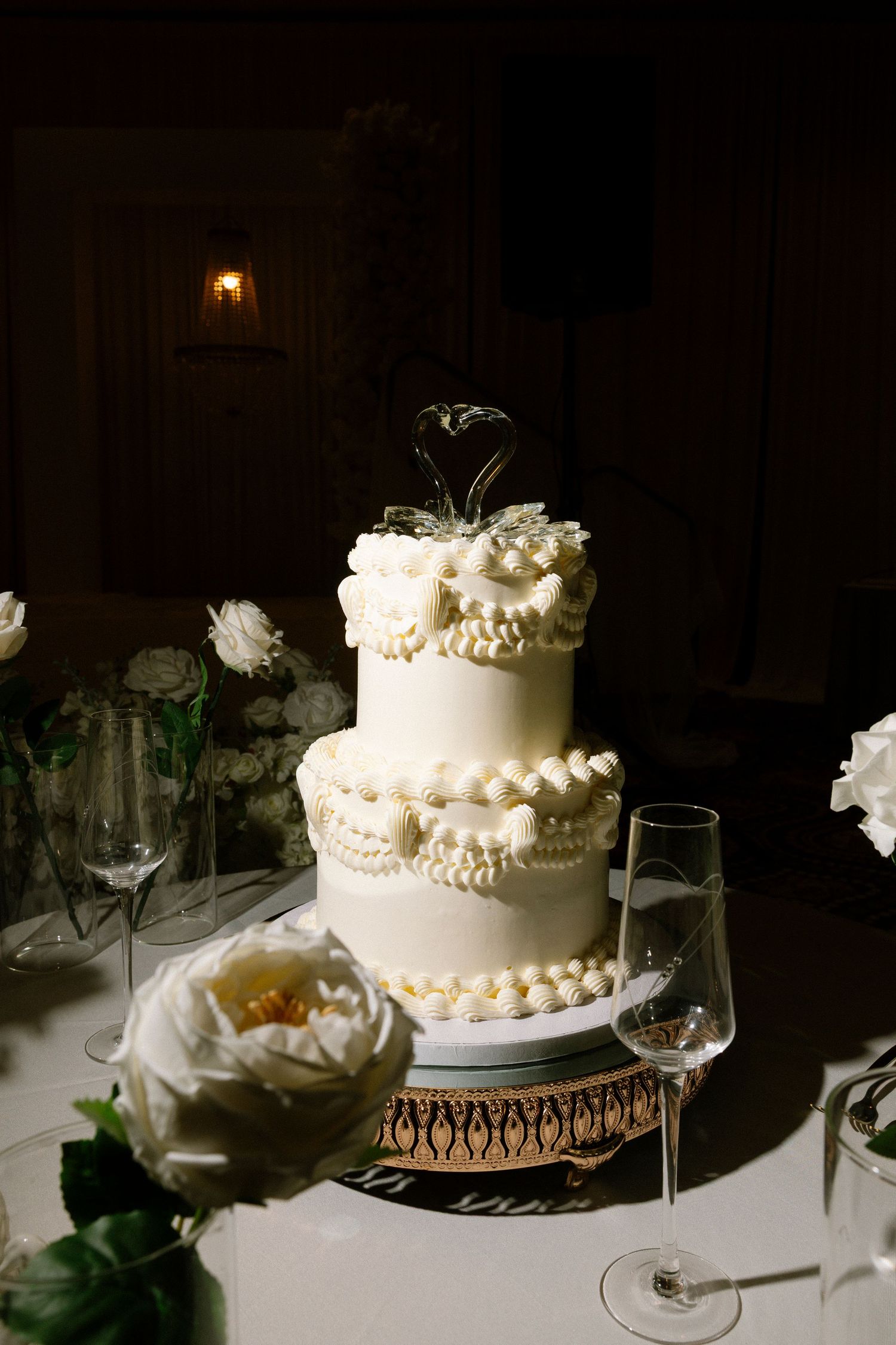 A series of elegant white wedding cakes with pearl decorations displayed on tables in a dimly lit reception venue.
