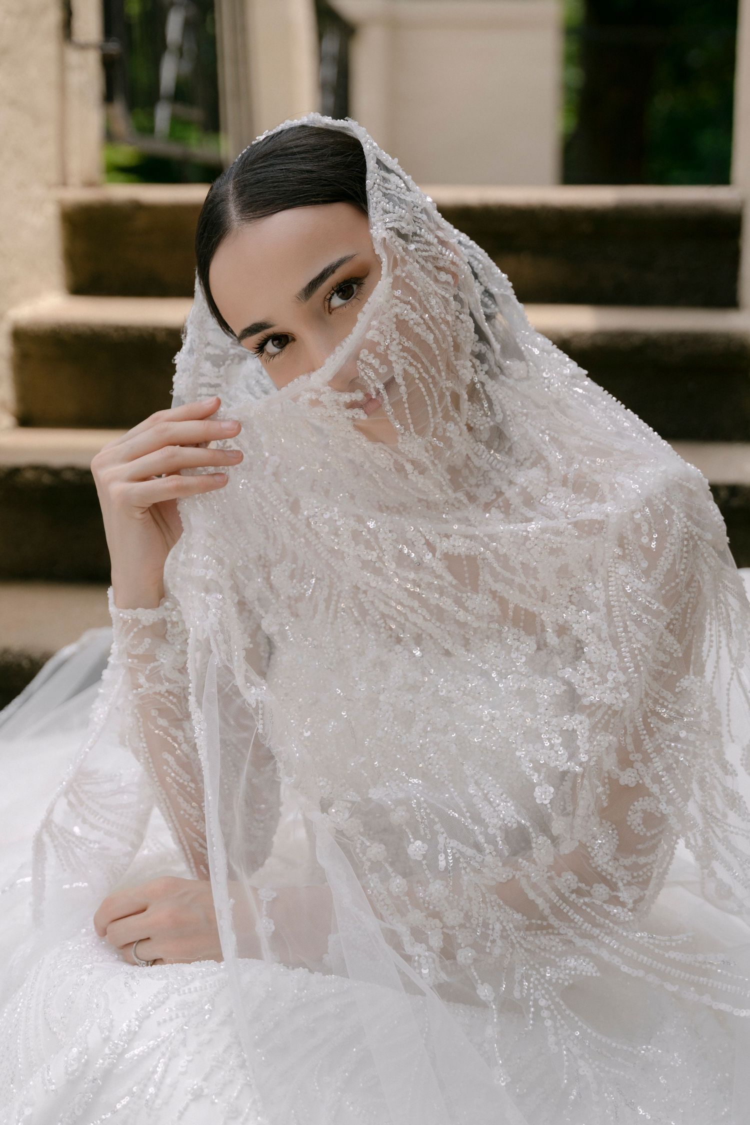 A bride in a delicate lace veil poses elegantly in a series of romantic wedding portraits outdoors.