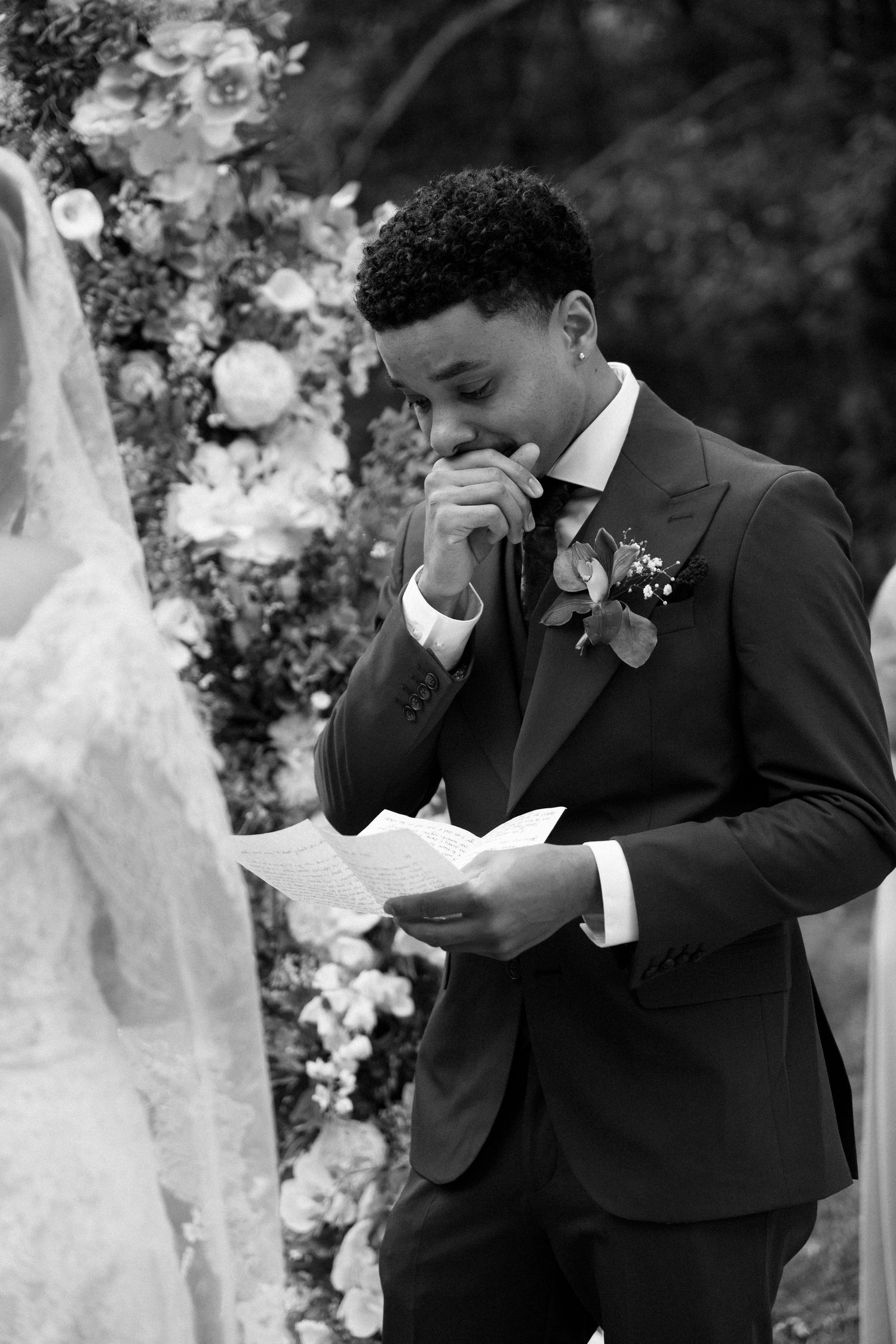 An emotional moment captured in black and white during an outdoor wedding ceremony with floral decorations.