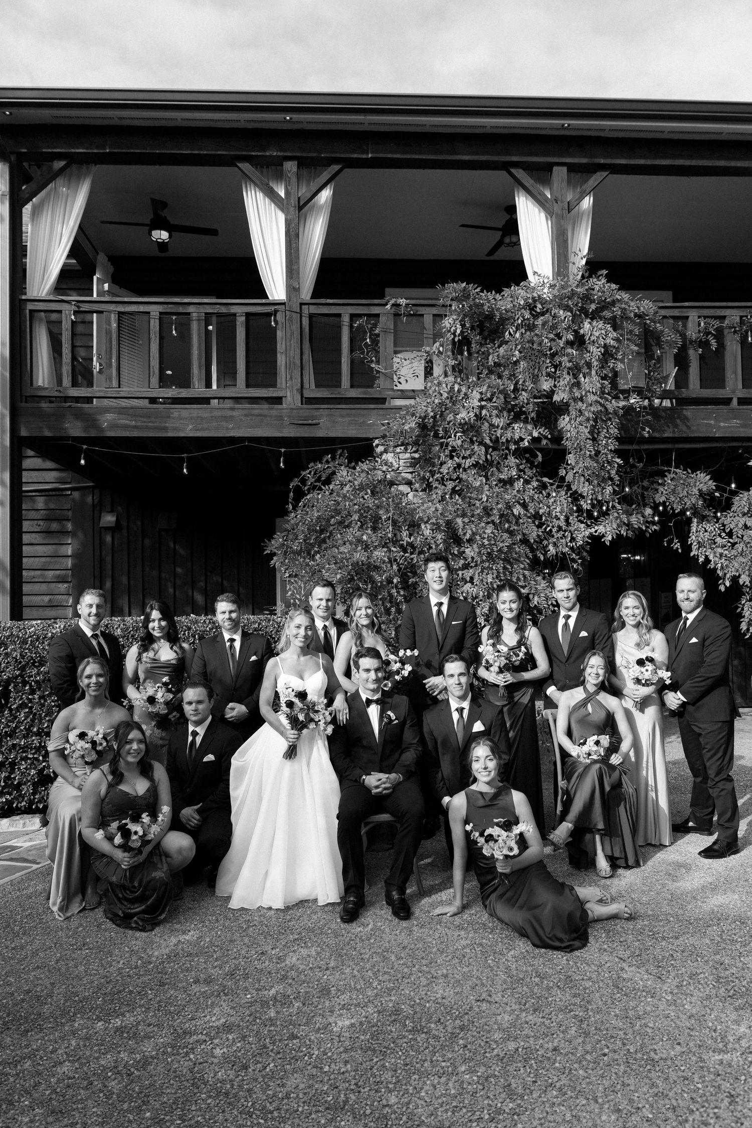 A black and white photo of a wedding party posing together on a grassy lawn.