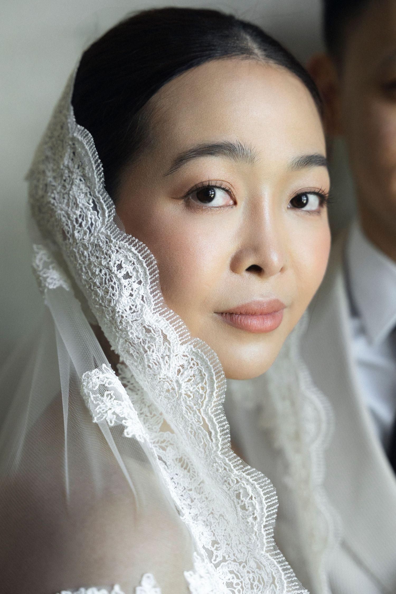 A close-up bridal portrait showing delicate white lace veil details against a soft neutral background.