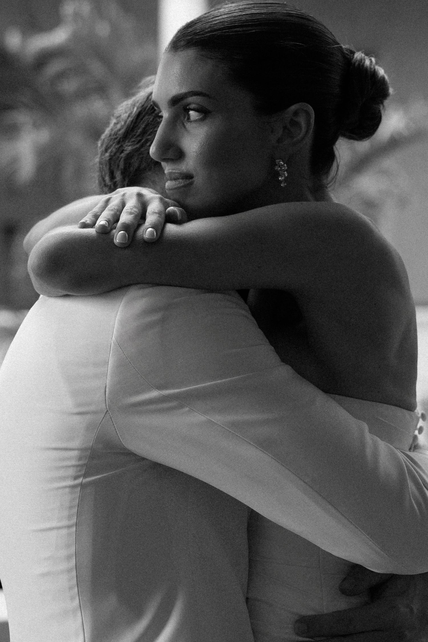 Black and white photo of a bride in a white gown sharing an emotional embrace at her wedding ceremony.
