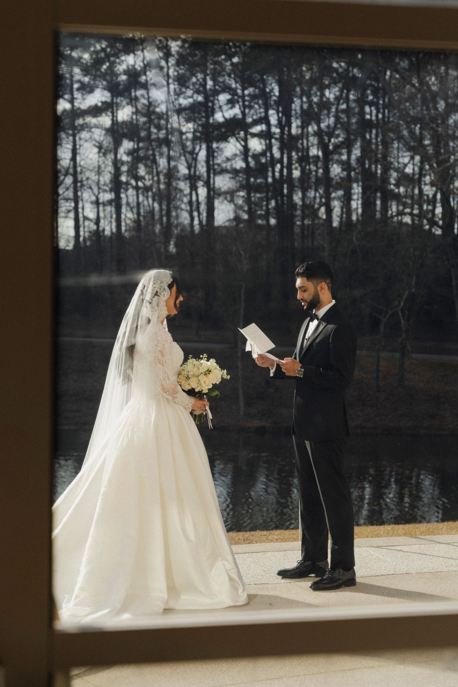 A couple exchanges vows during their wedding ceremony on a deck overlooking a serene lake surrounded by pine trees.
